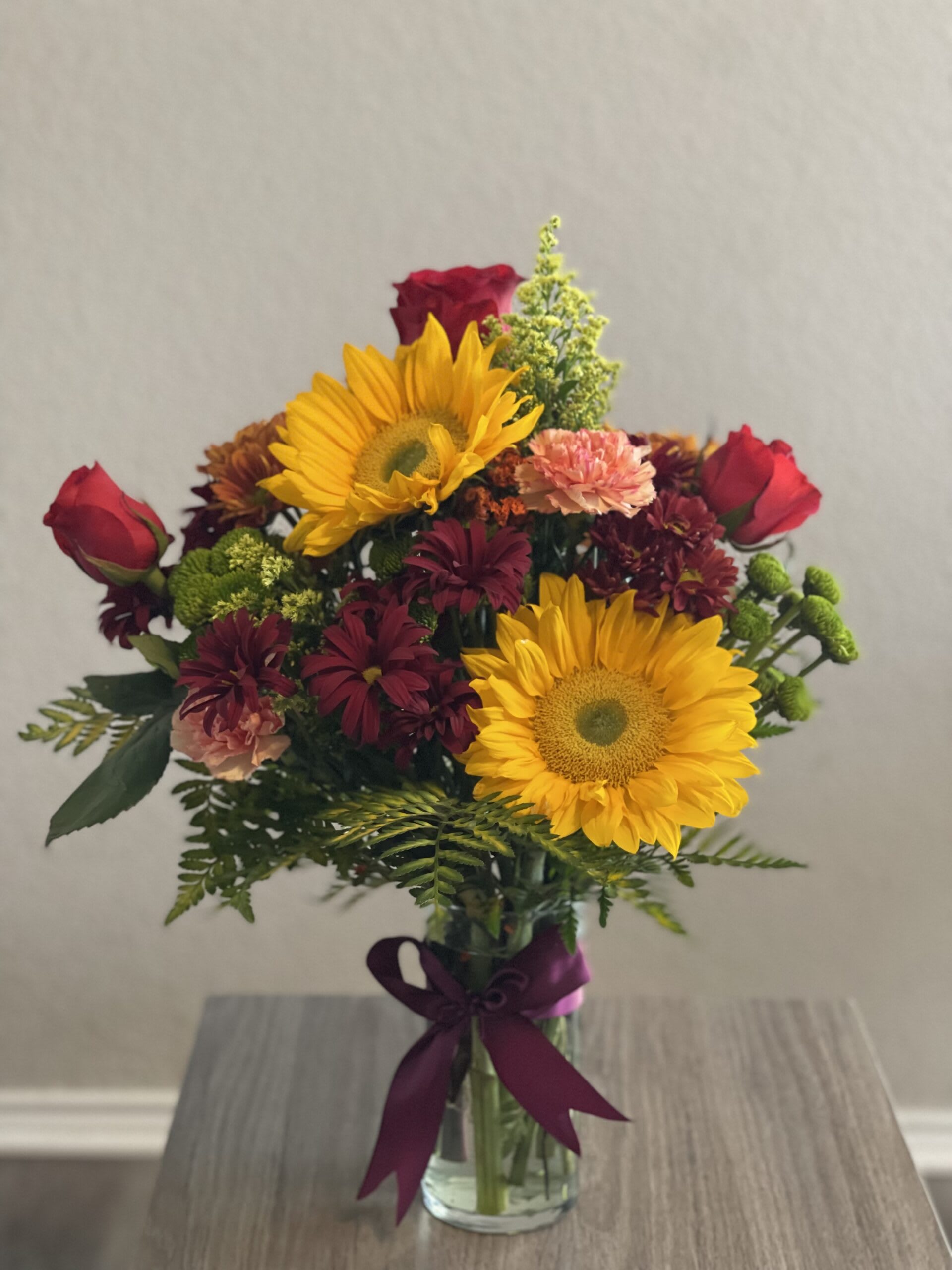 Bouquet of sunflowers, red roses, and mixed blooms in a glass vase