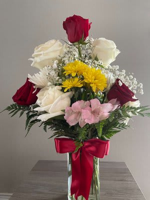 Mixed bouquet of roses, daisies, and pink flowers in a glass vase with a red bow
