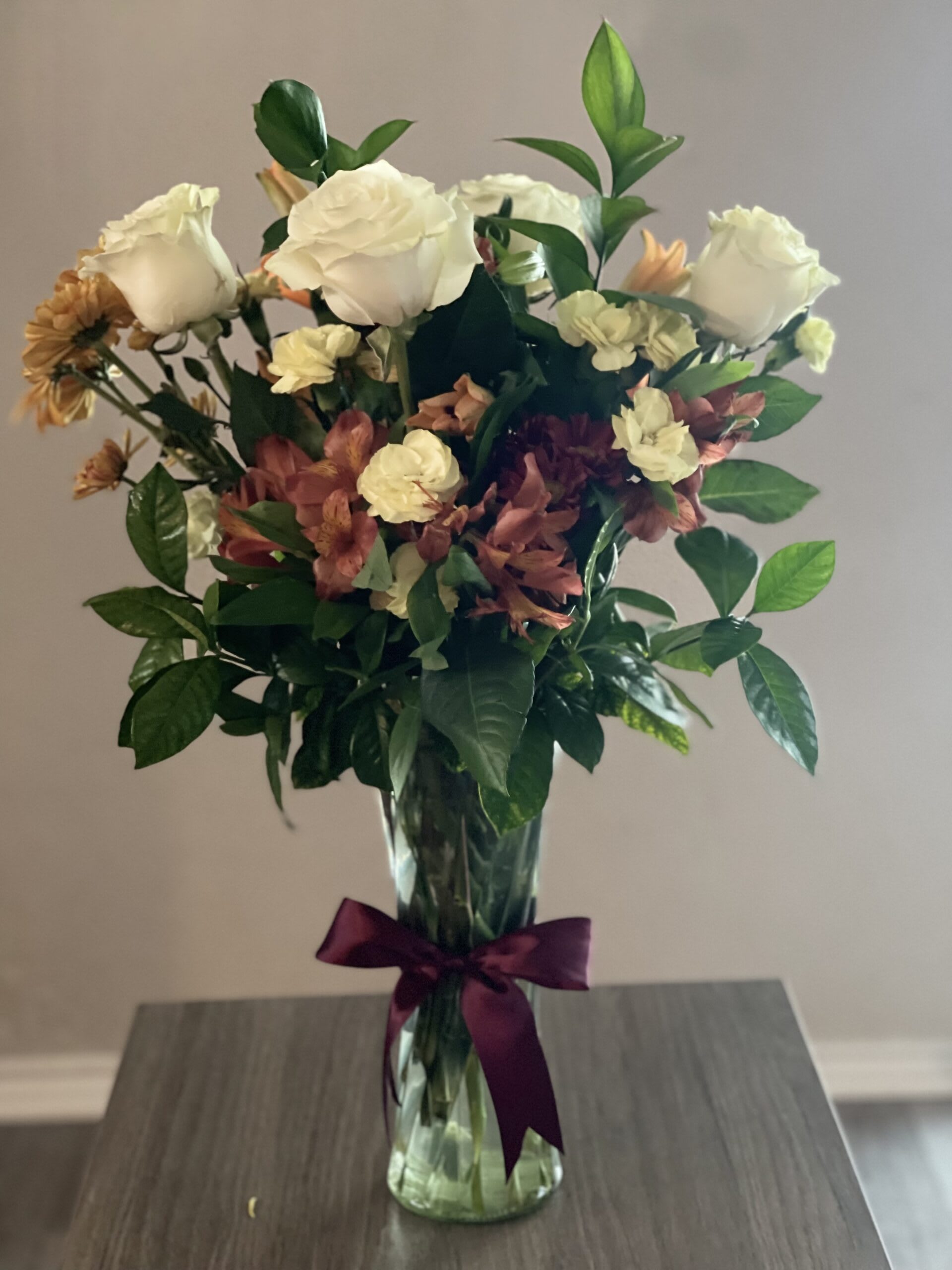 Bouquet of white roses and mixed flowers in a glass vase with a purple ribbon