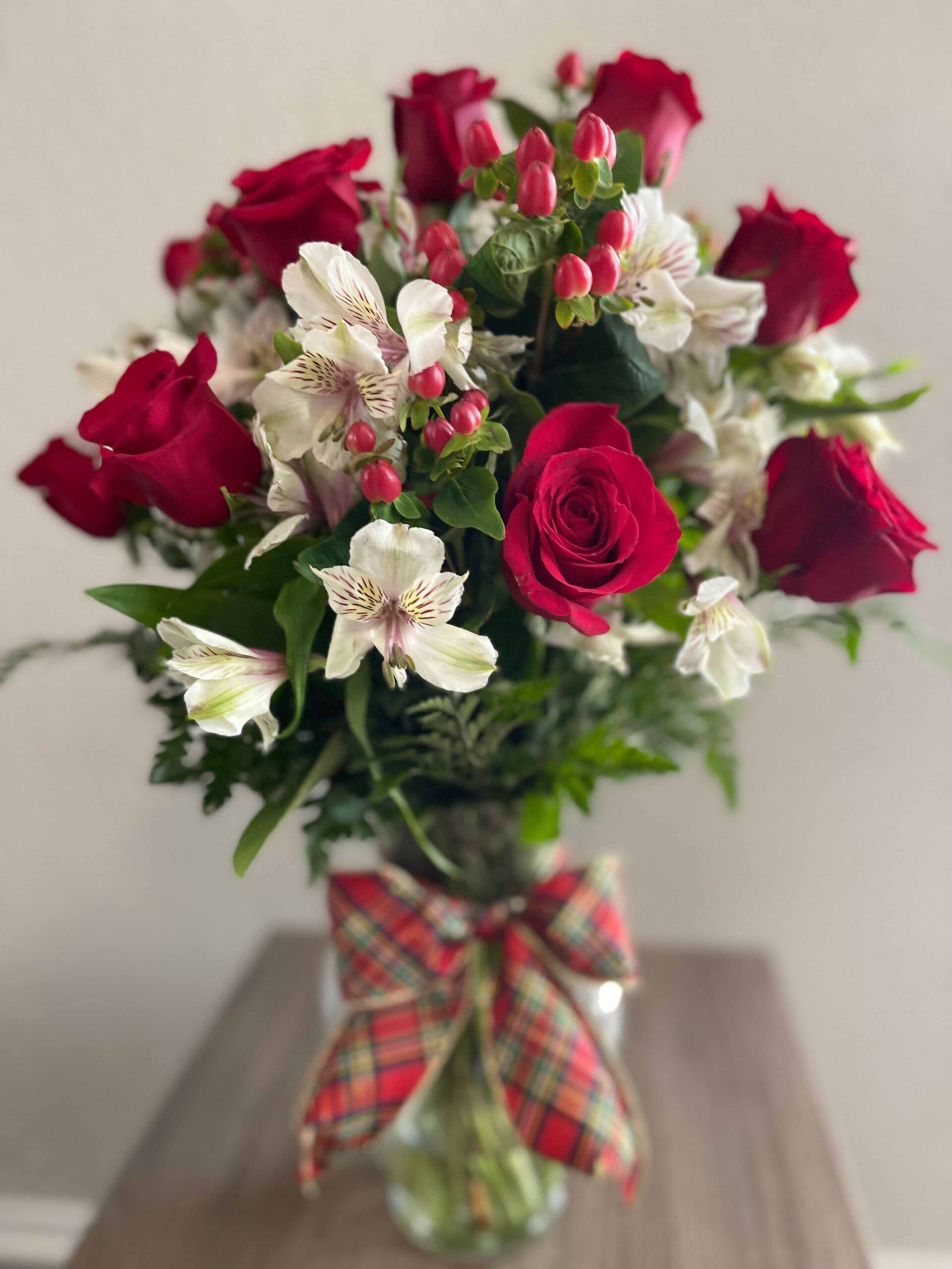 Bouquet of red roses and white alstroemeria in a glass vase with plaid ribbon