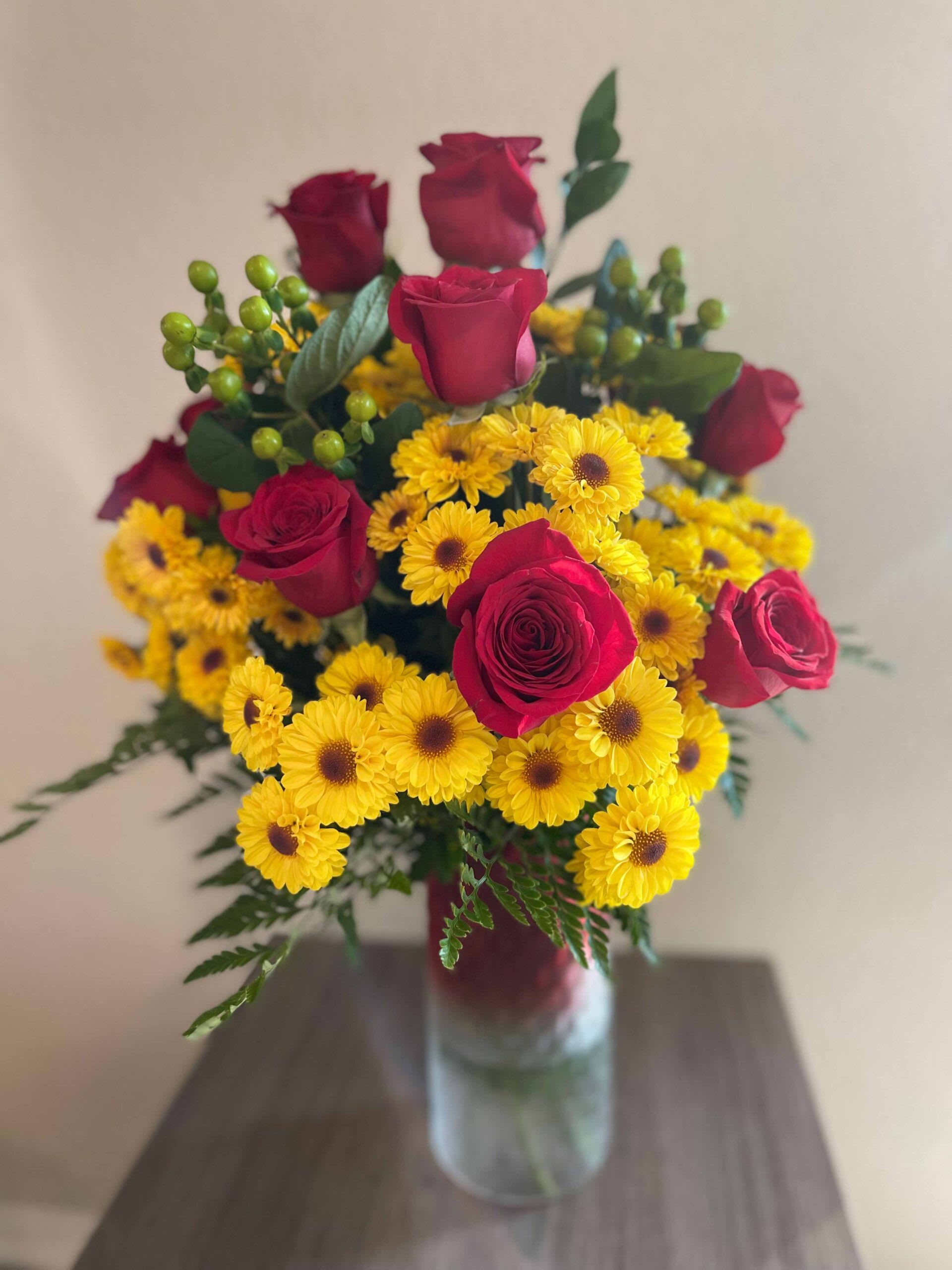 Bouquet of red roses and yellow daisies in a clear glass vase