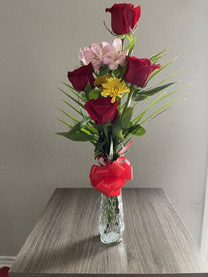 Tall bouquet of red roses and pink flowers in a glass vase with a red bow