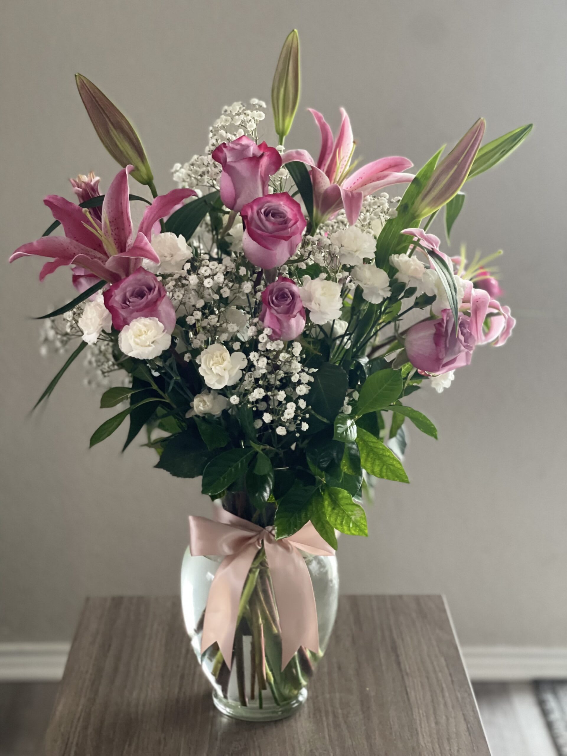 Pink lilies and roses in a glass vase with a ribbon