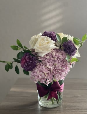 Pink hydrangea and white roses in a glass vase with purple blooms