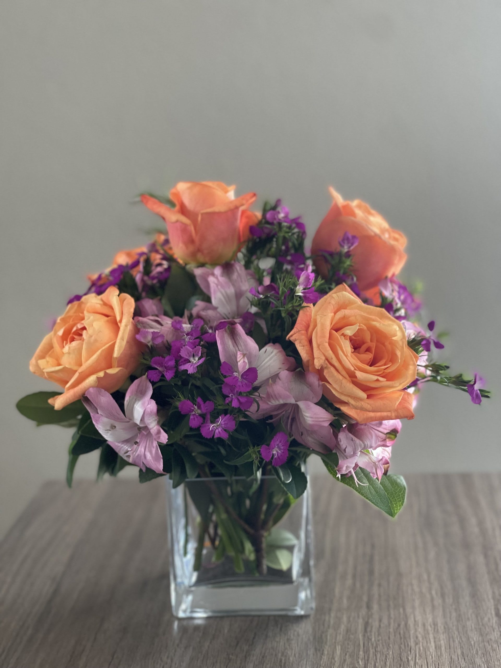 Peach roses and purple flowers in a clear glass vase