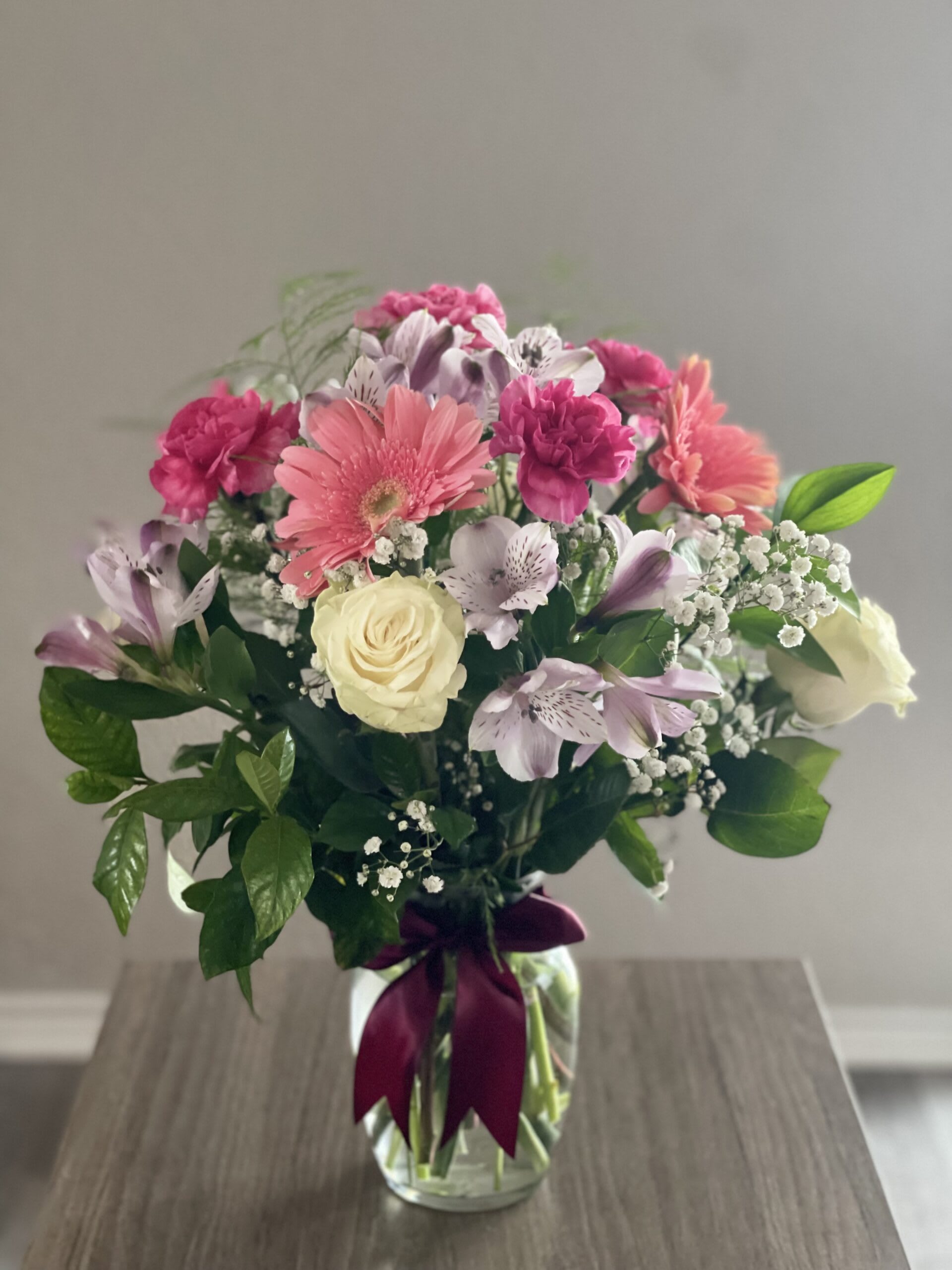 Mixed pink and white bouquet in a glass vase with a purple ribbon
