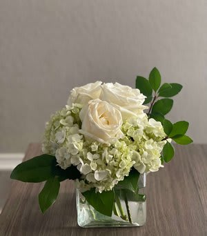White roses and pale hydrangeas in a clear square vase