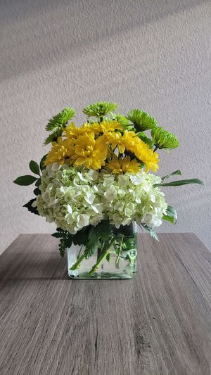 Yellow and pale green flowers arranged in a clear square vase