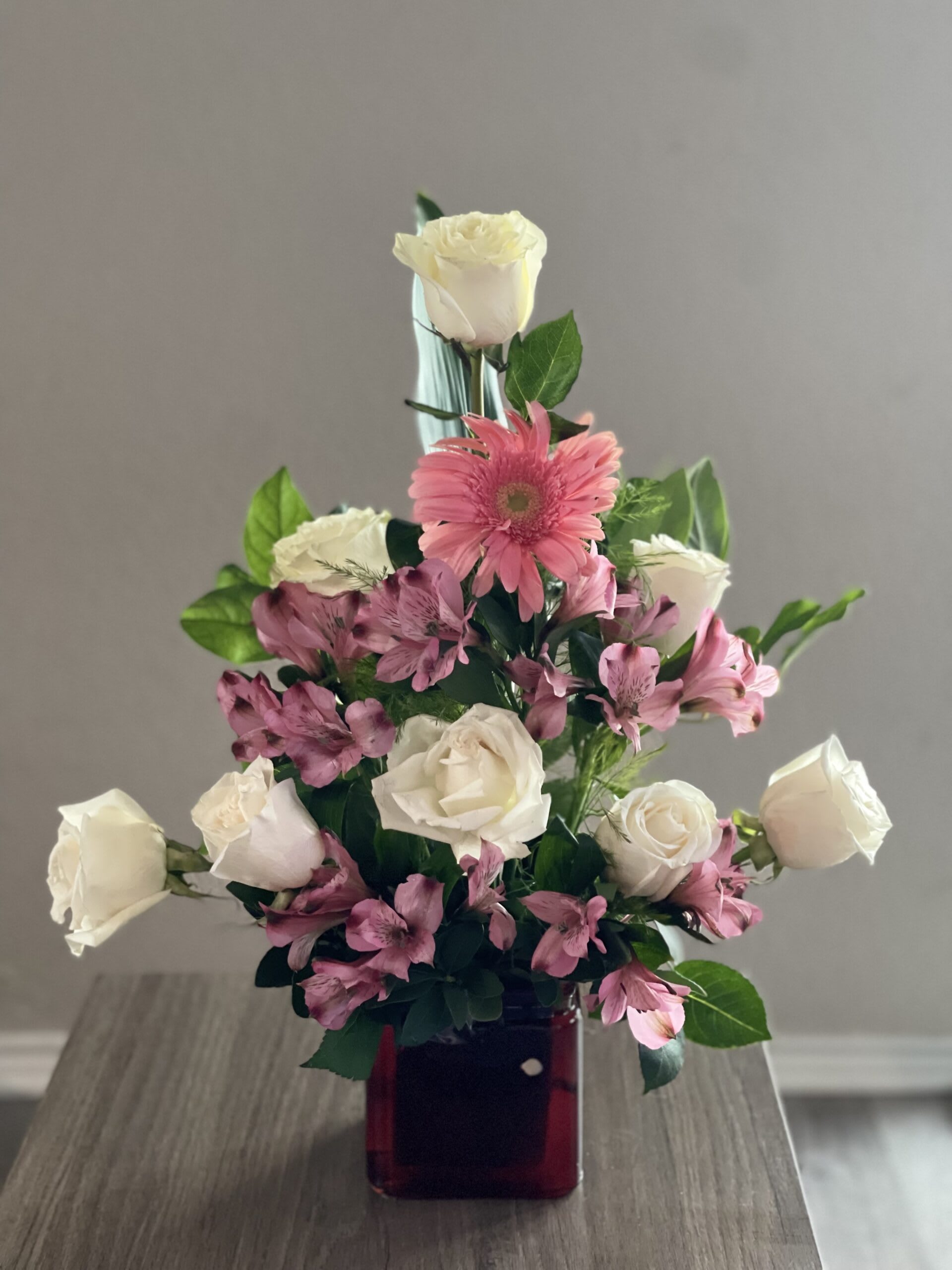 Pink and white roses with pink alstroemeria in a red glass vase