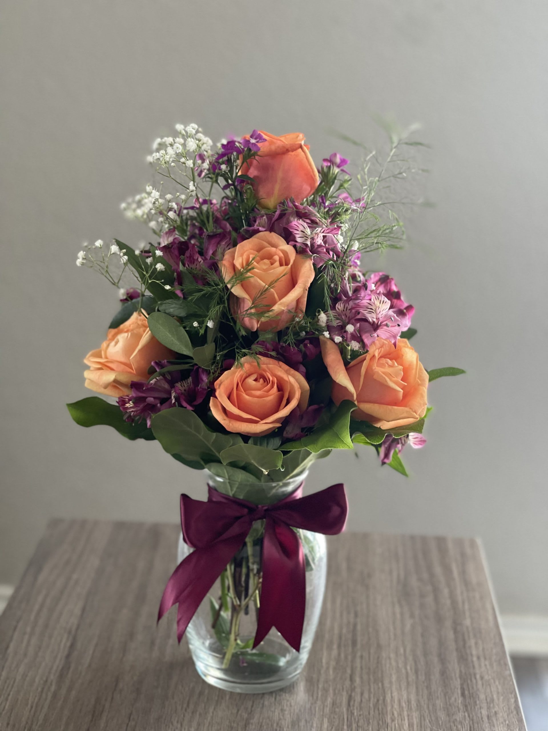 Peach roses and purple flowers in a glass vase with a ribbon