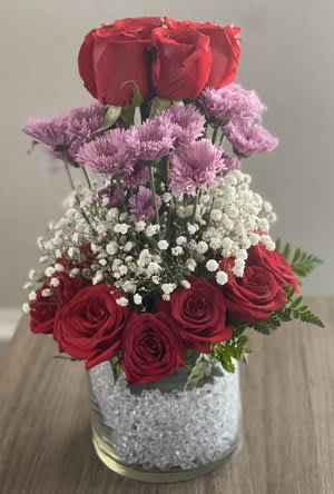 Red roses and purple flowers arranged in a glass vase