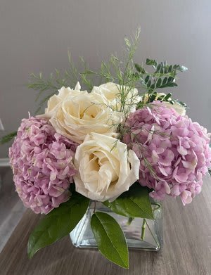 White roses and pink hydrangeas in a square glass vase