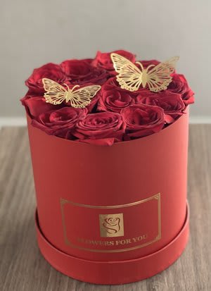 Red roses arranged in a round red box with butterfly toppers
