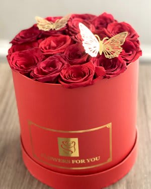 Red roses arranged in a round red box with butterfly decorations