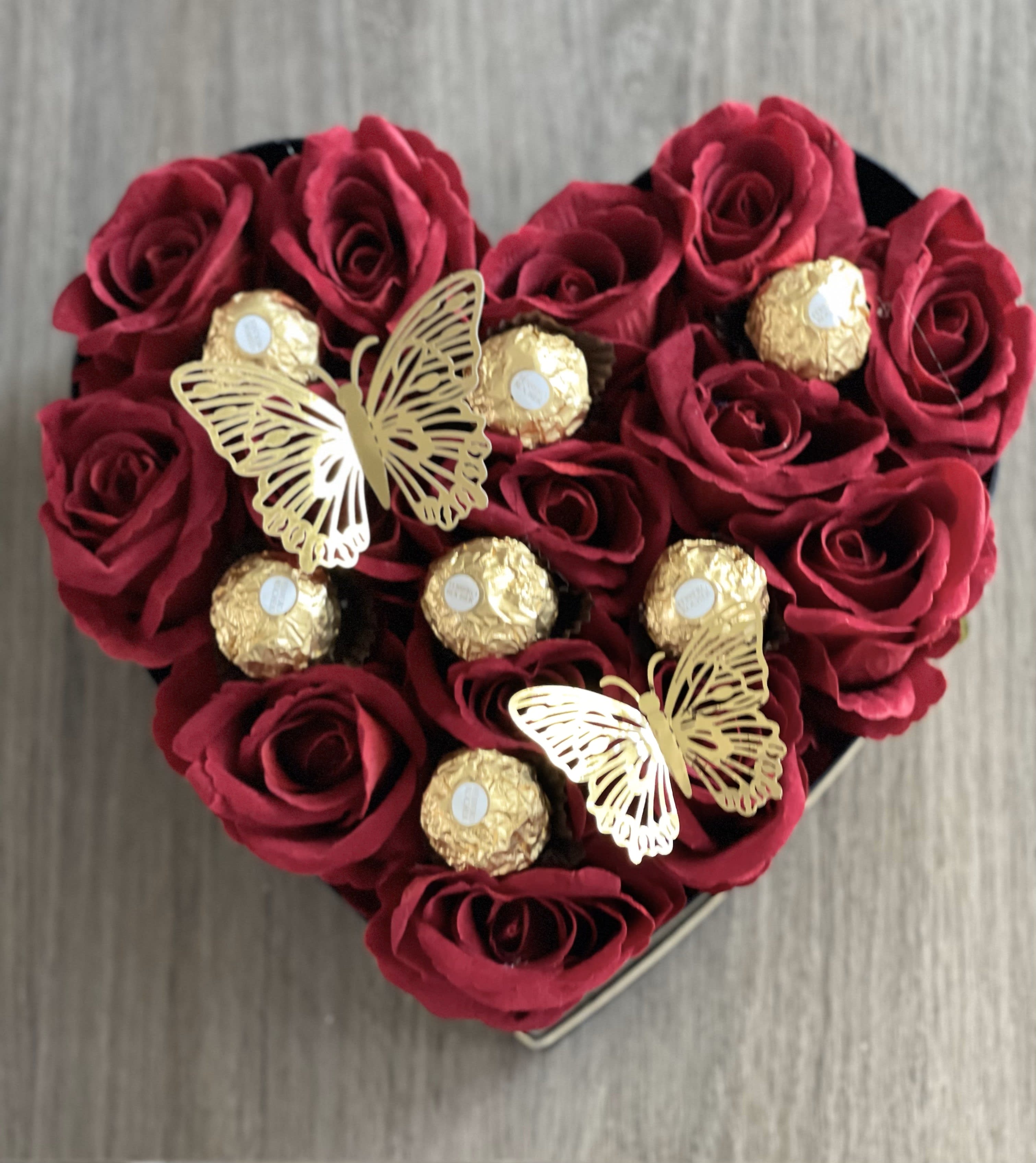 Heart-shaped box of red roses with gold-wrapped chocolates and butterfly decorations