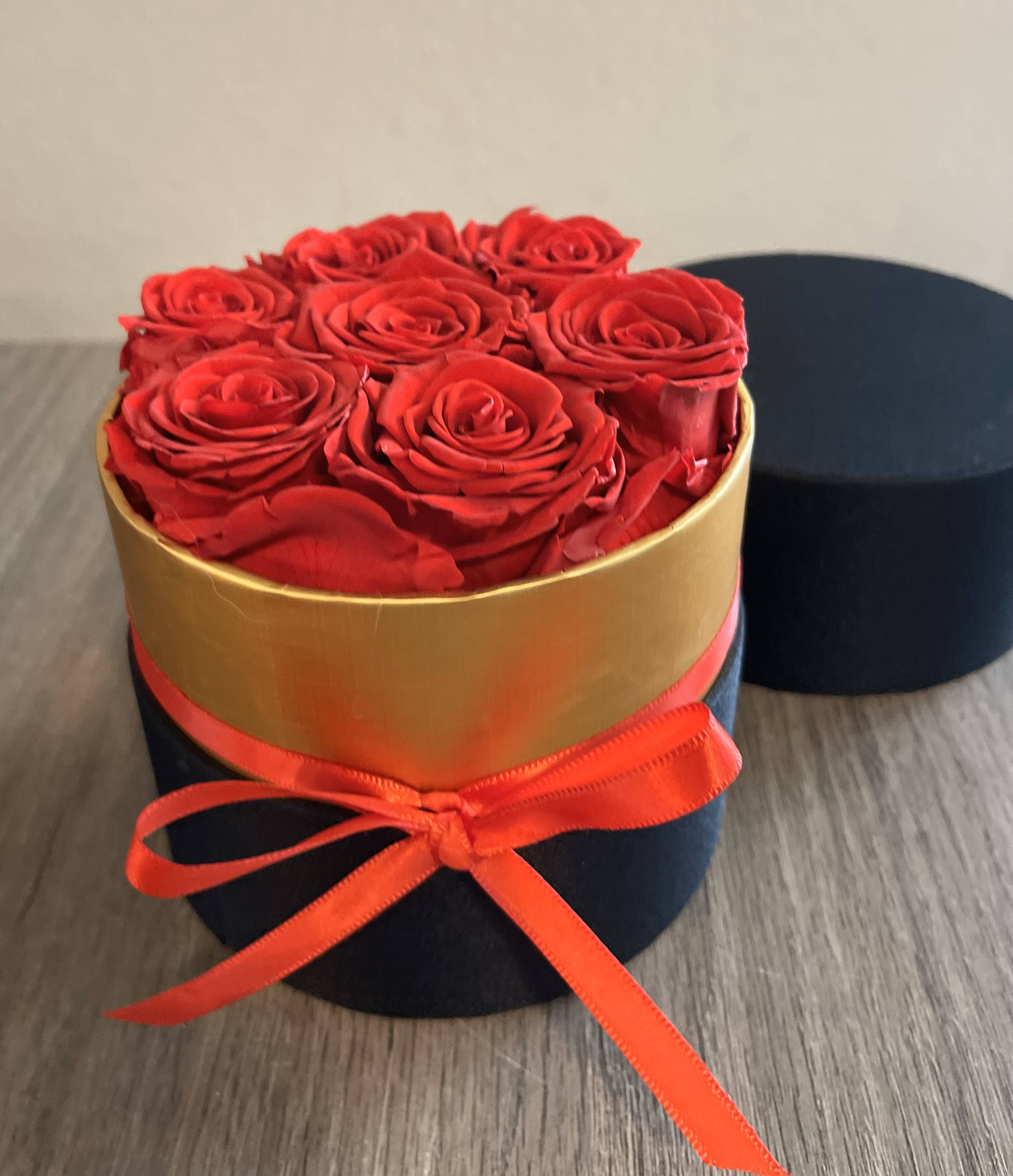 Red roses arranged in a round black box with a gold band and red ribbon