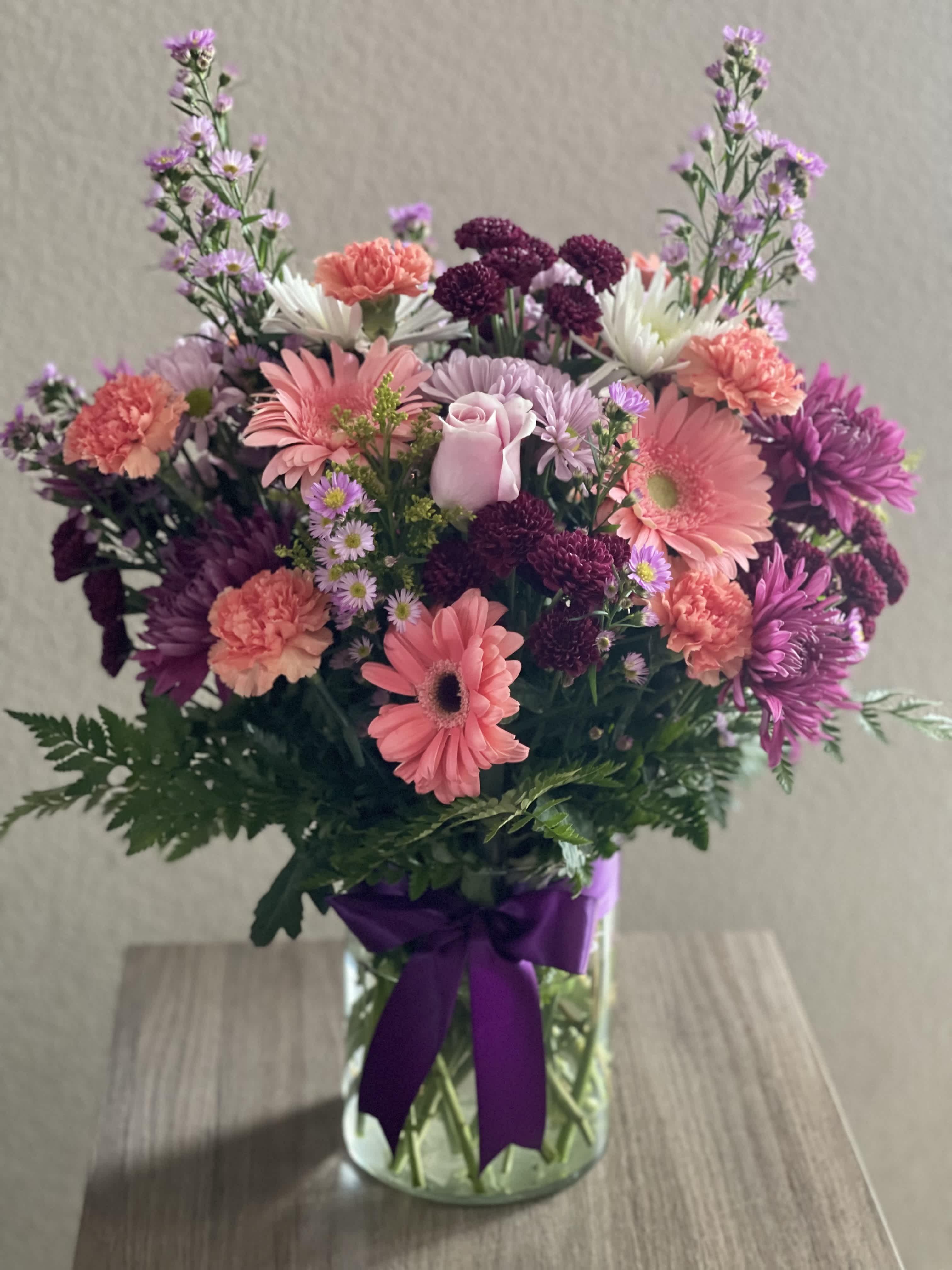 Mixed pink and purple bouquet in a glass vase with a purple ribbon