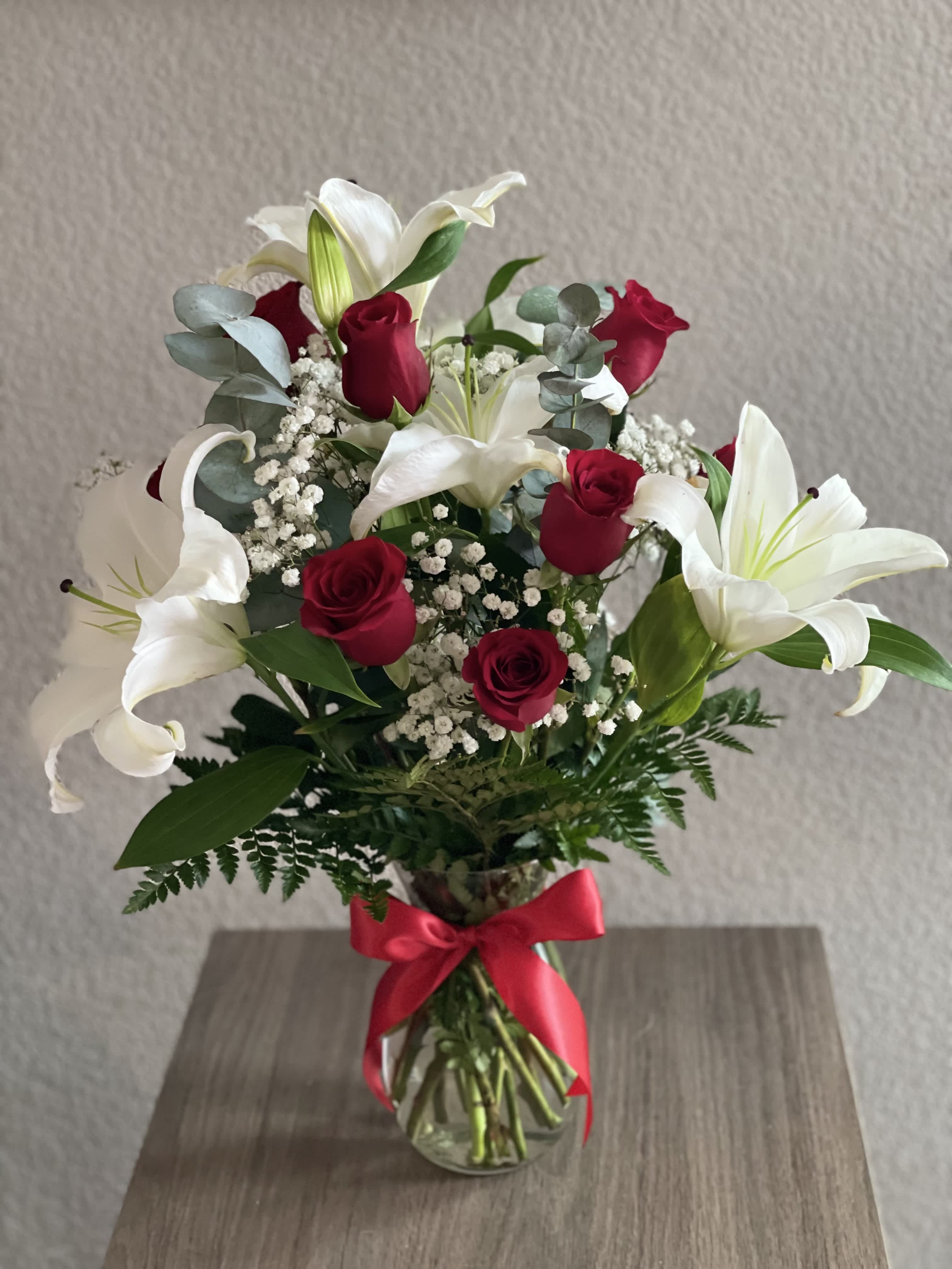 Bouquet of red roses and white lilies in a glass vase with a red ribbon