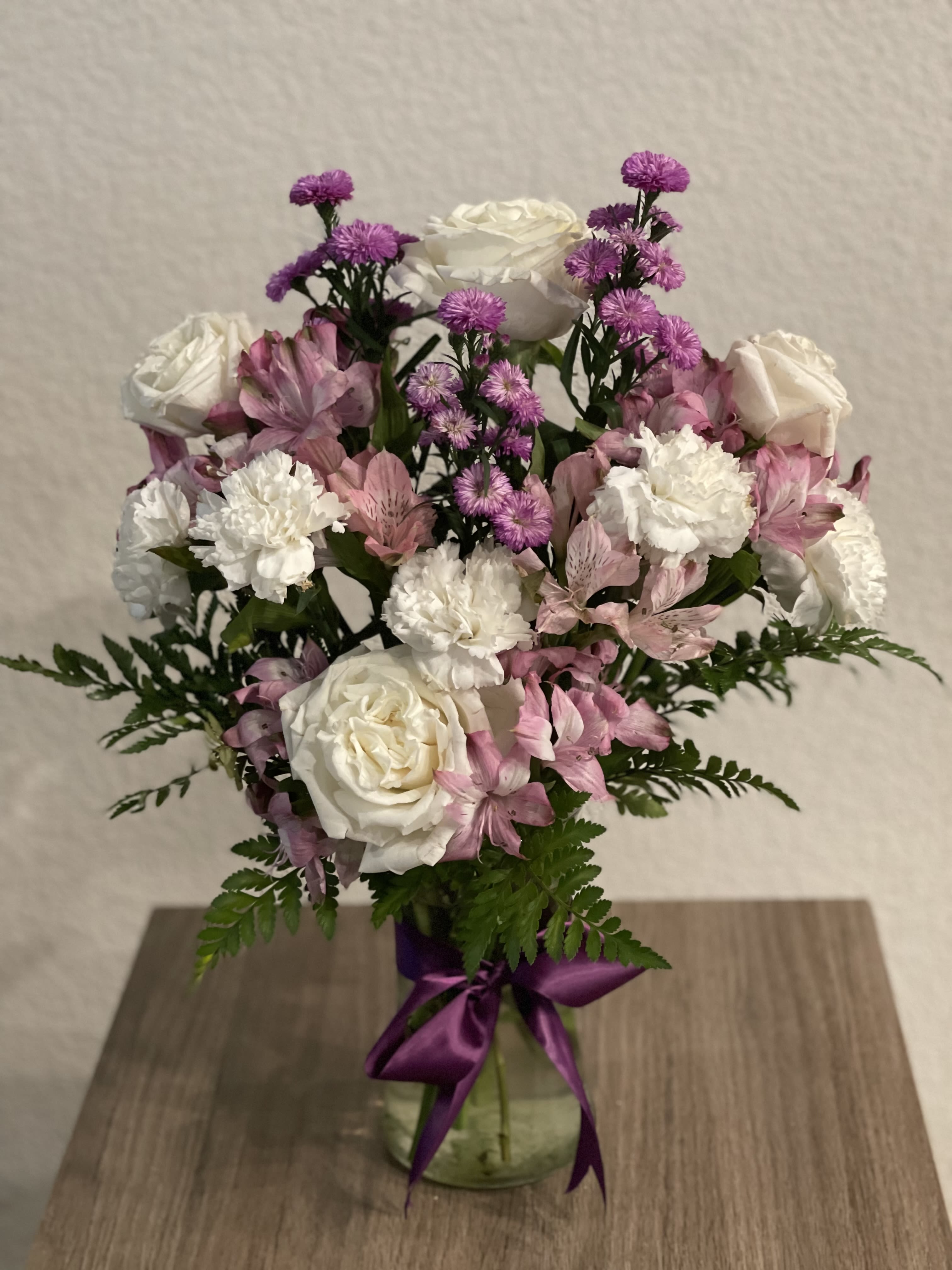 Pink and white bouquet in a glass vase with a purple ribbon