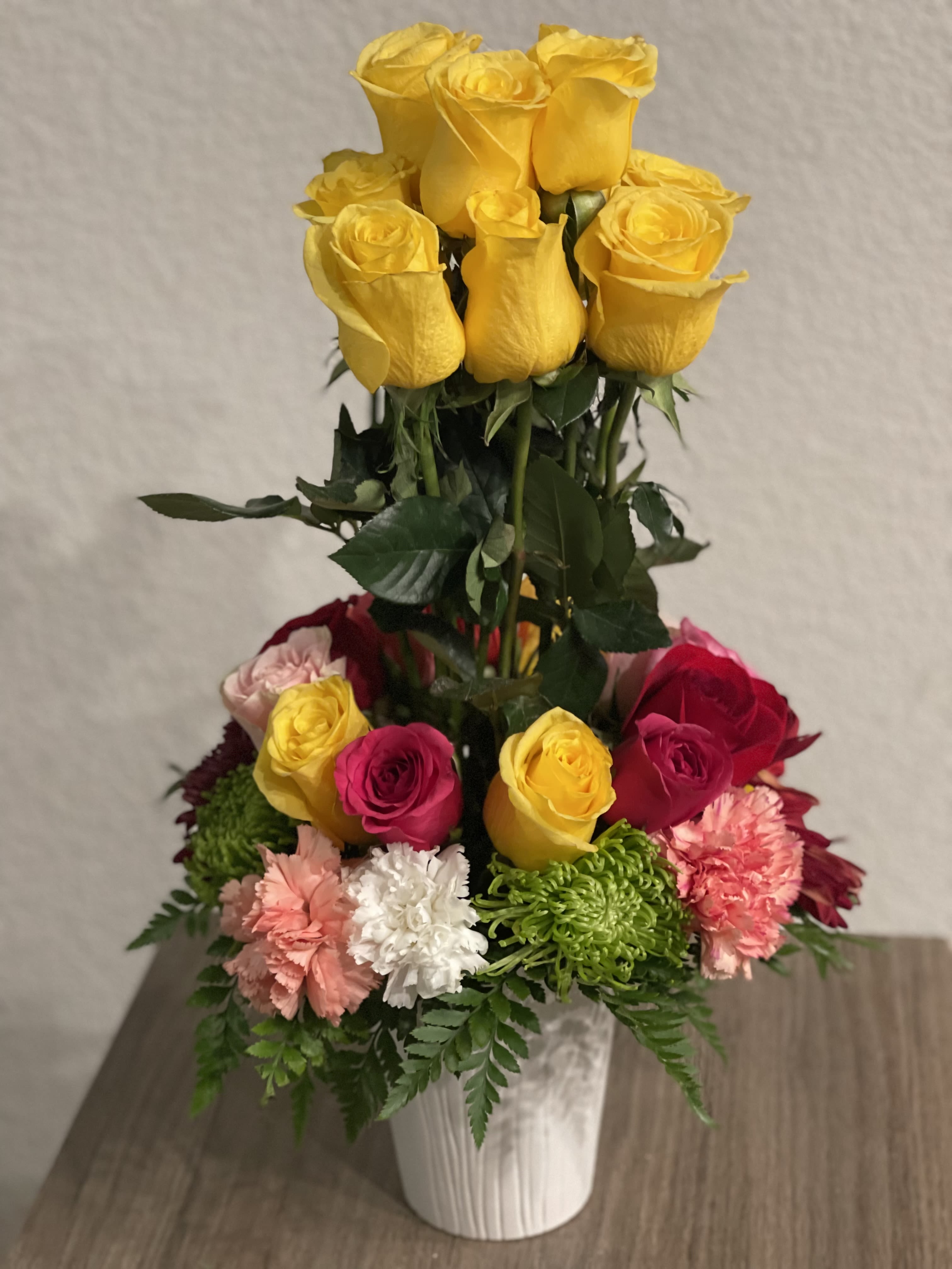 Tall bouquet of yellow and pink roses with carnations in a white vase