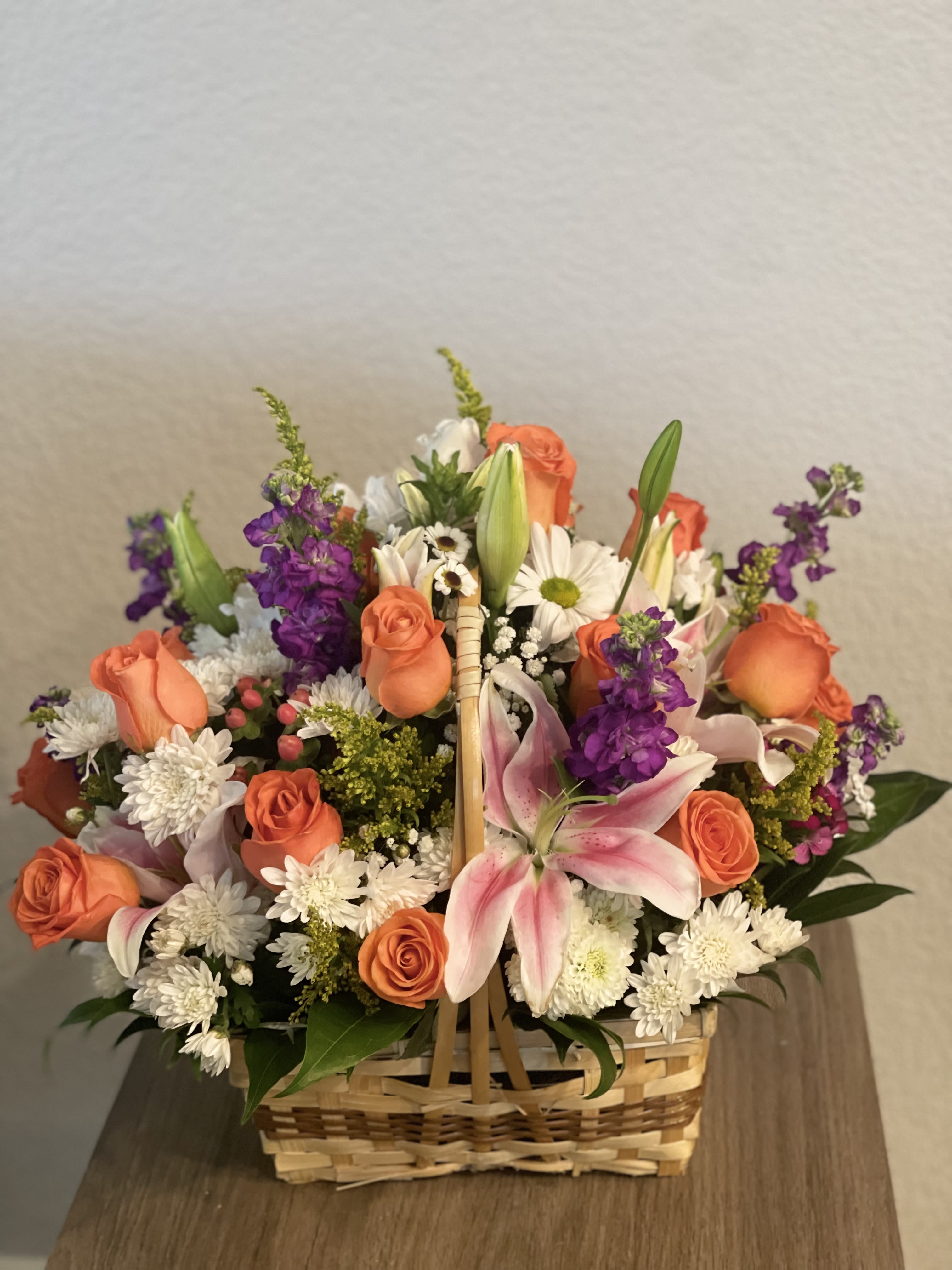 Basket arrangement of orange roses, pink lilies, and white daisies