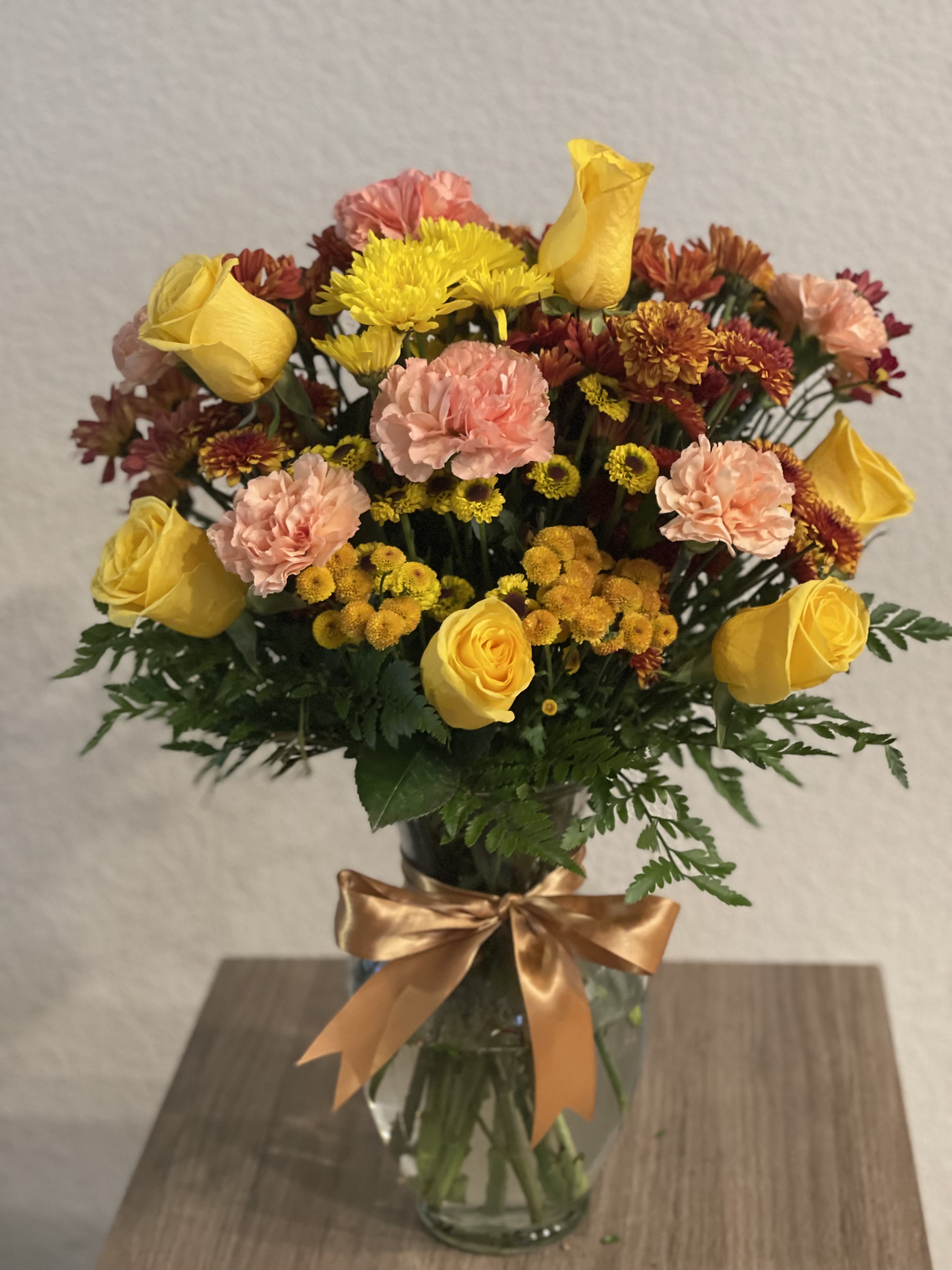 Yellow roses and pink carnations in a glass vase with a gold ribbon