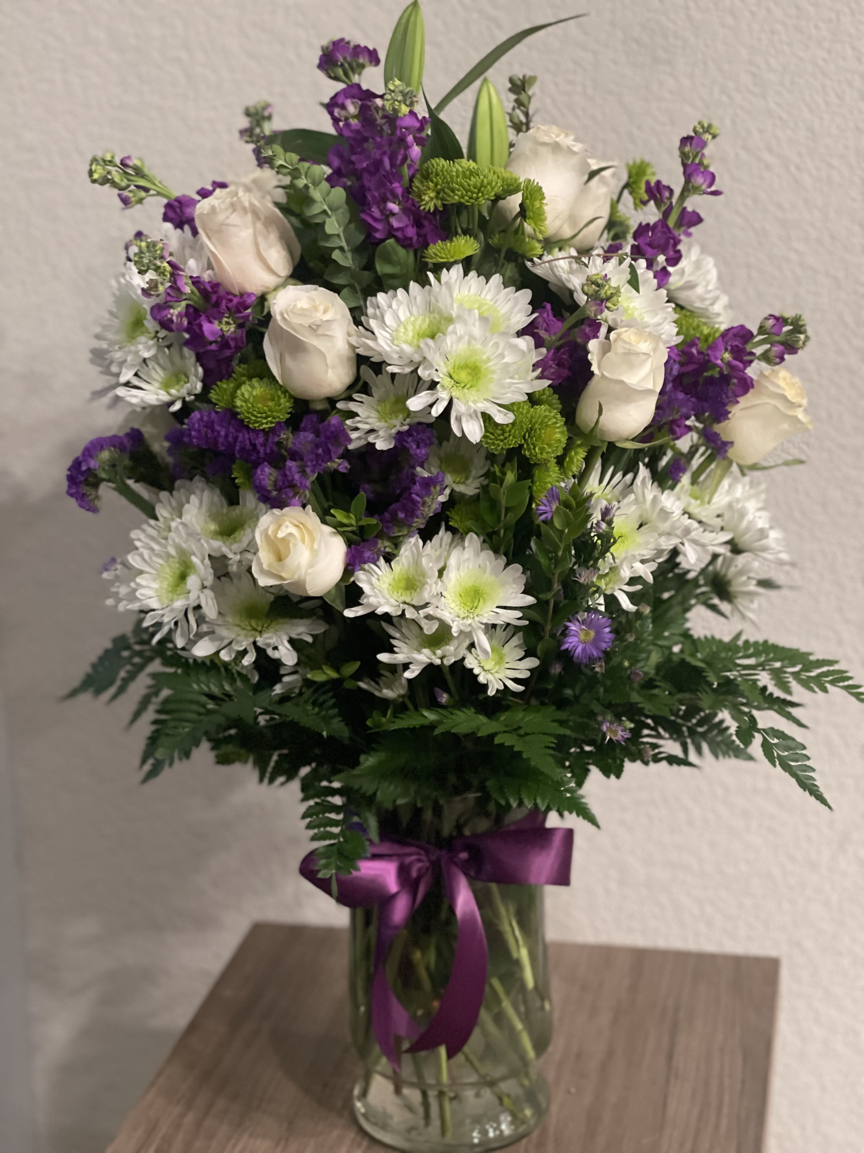 Bouquet of white roses, white daisies, and purple flowers in a glass vase