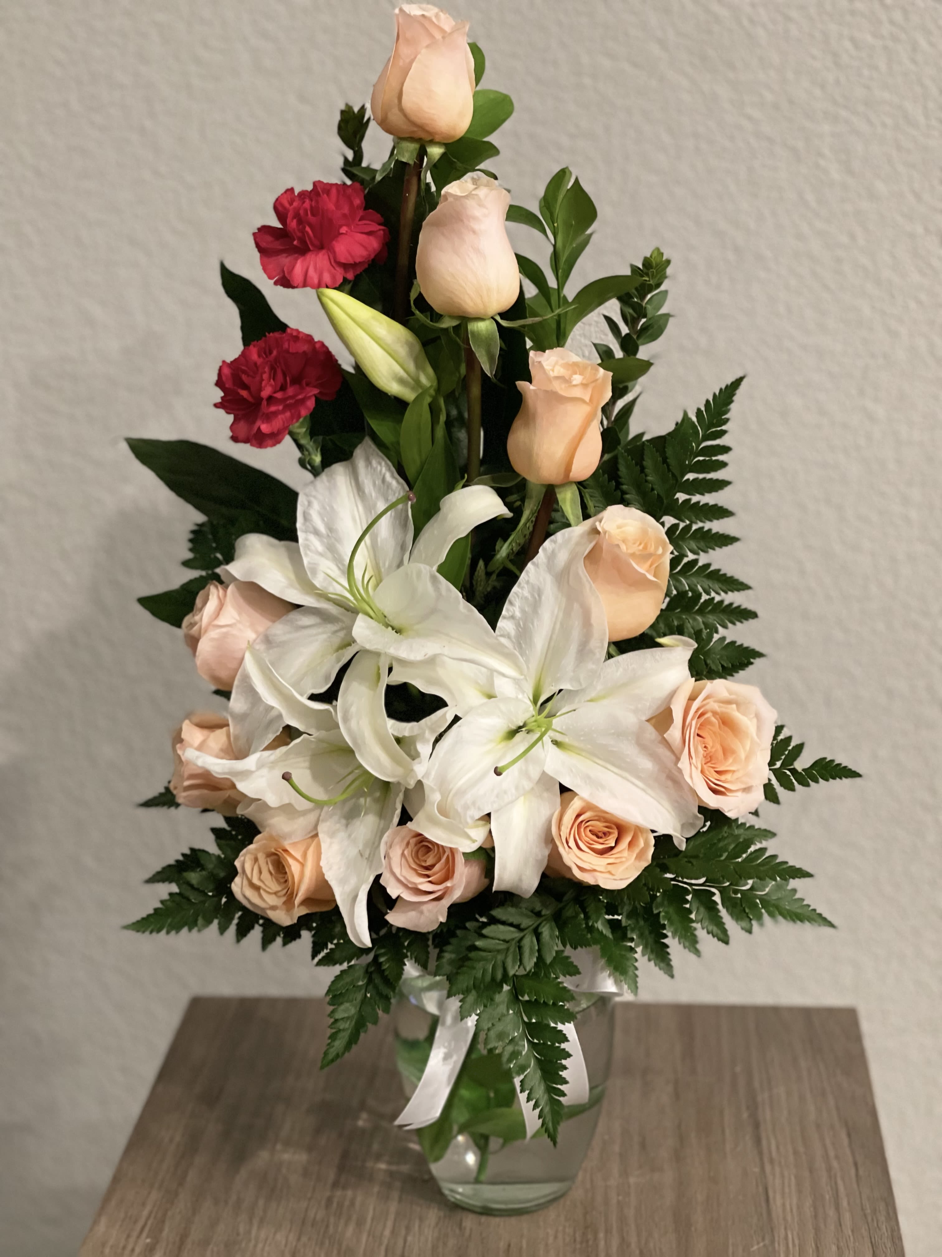 Bouquet of peach roses, white lilies, and red carnations in a glass vase