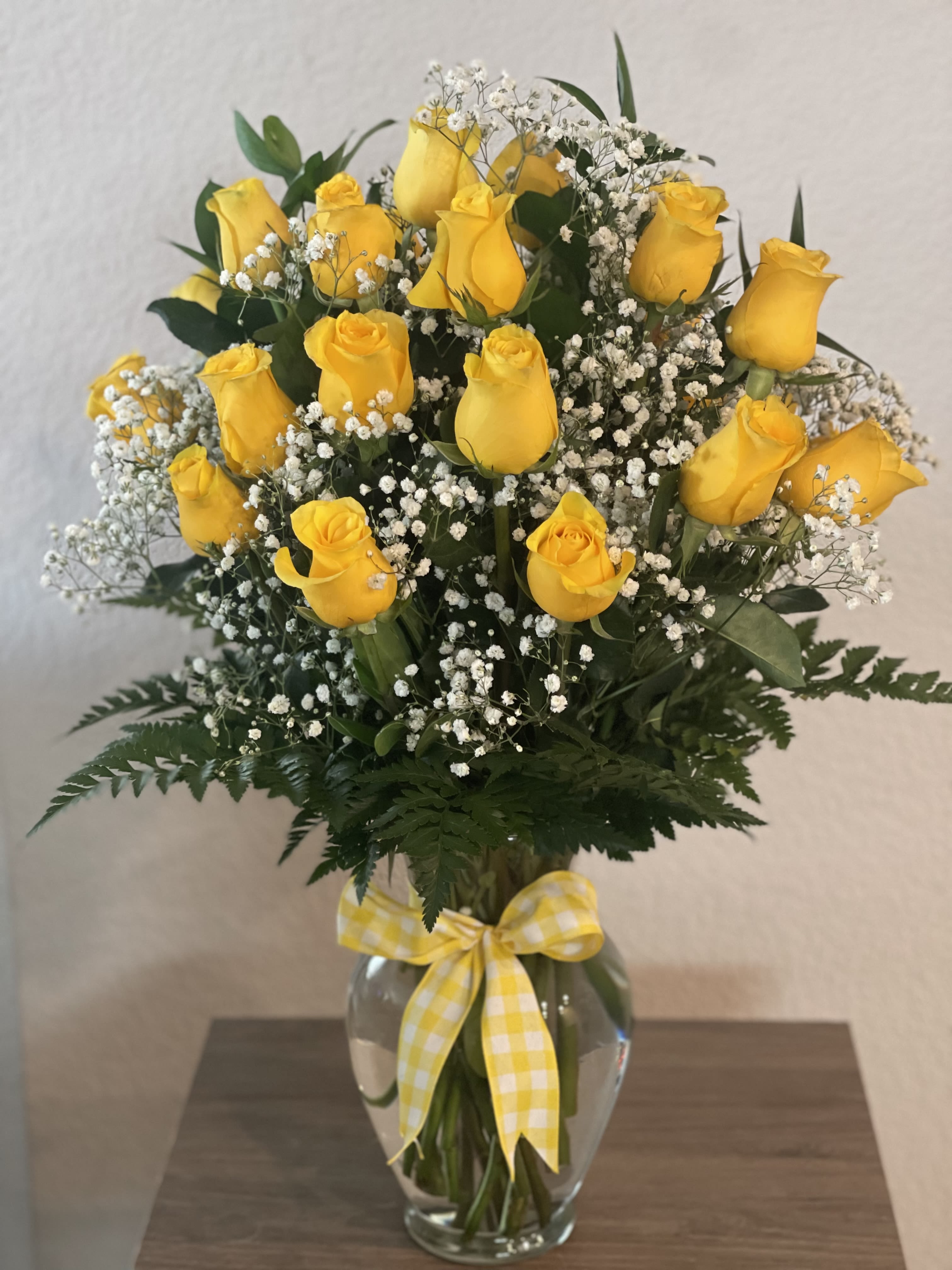 Yellow roses in a clear glass vase with white baby's breath and a gingham ribbon