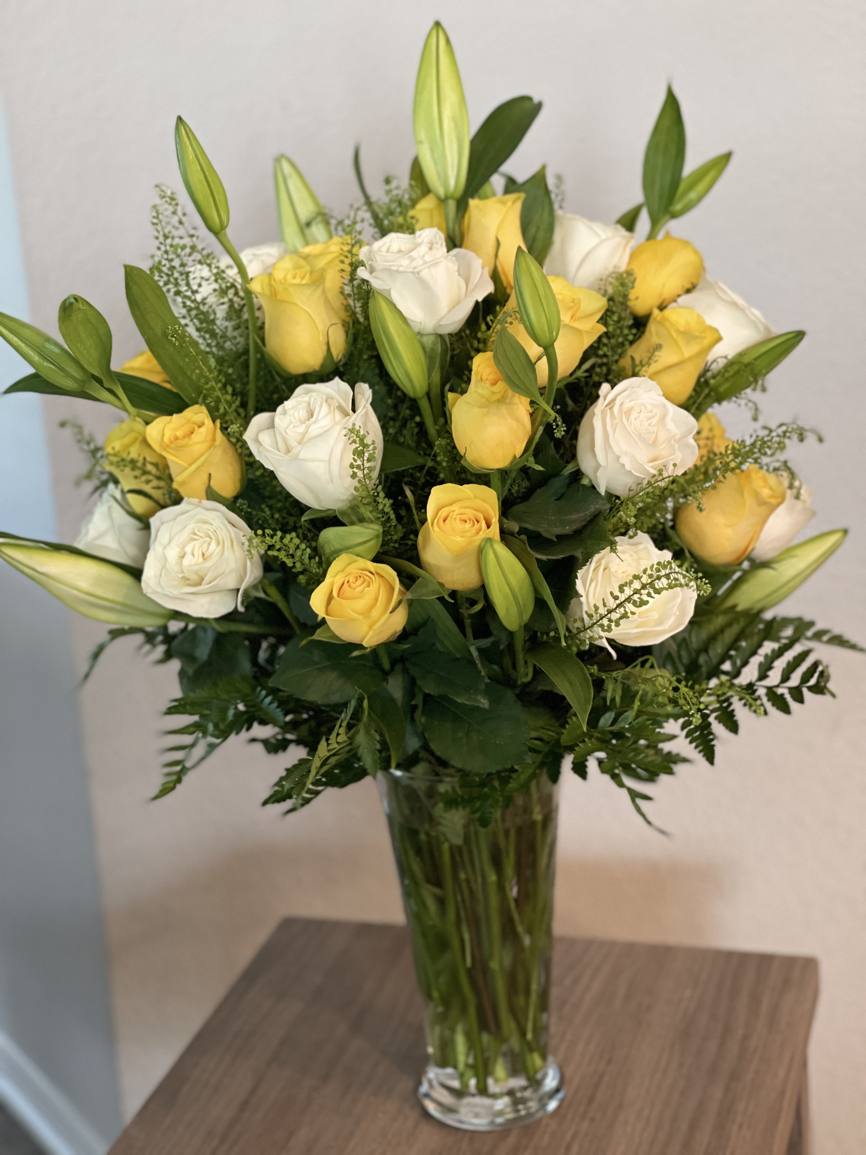 Yellow and white roses arranged in a tall glass vase