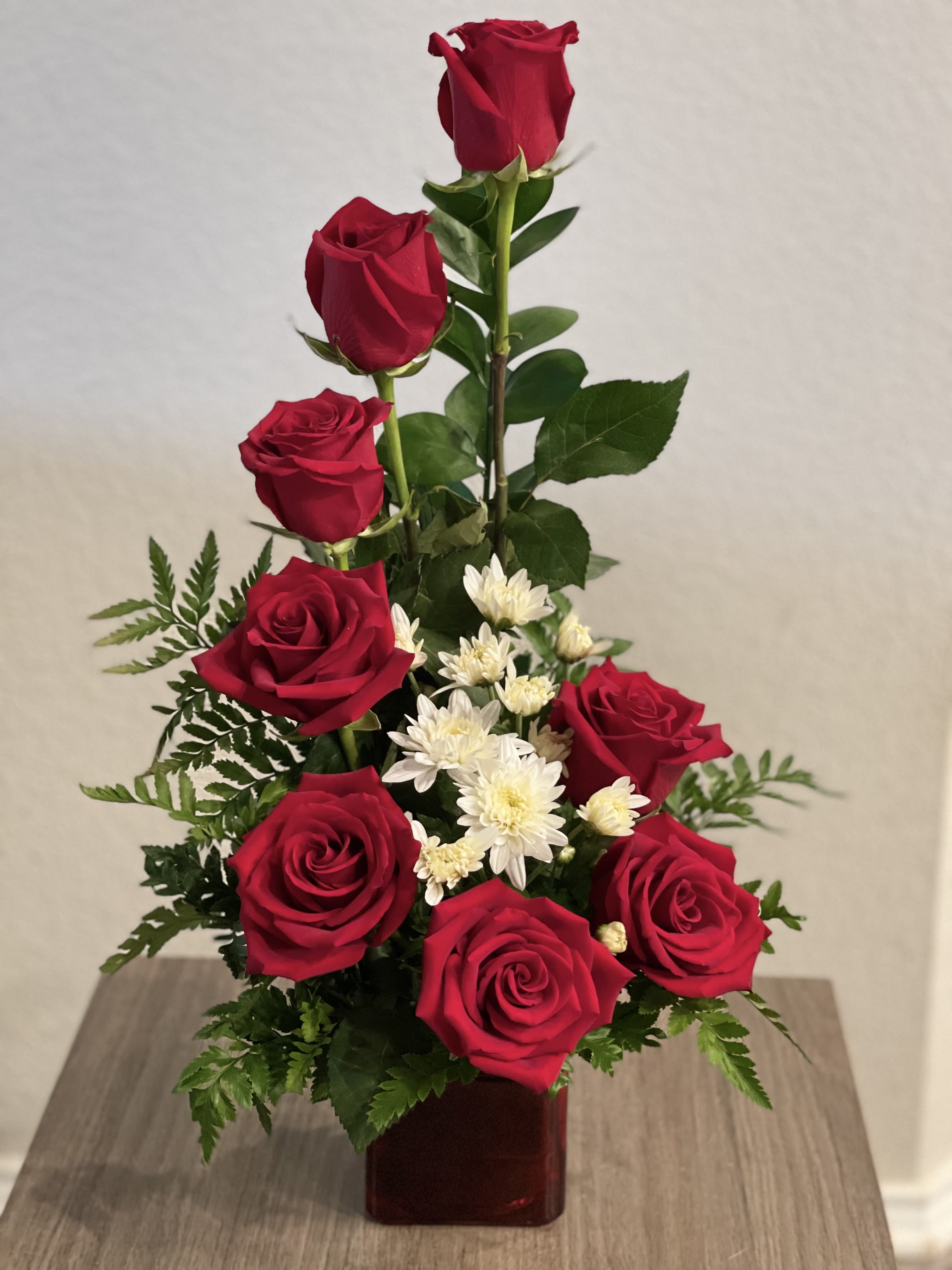 Red roses and white daisies arranged in a square vase