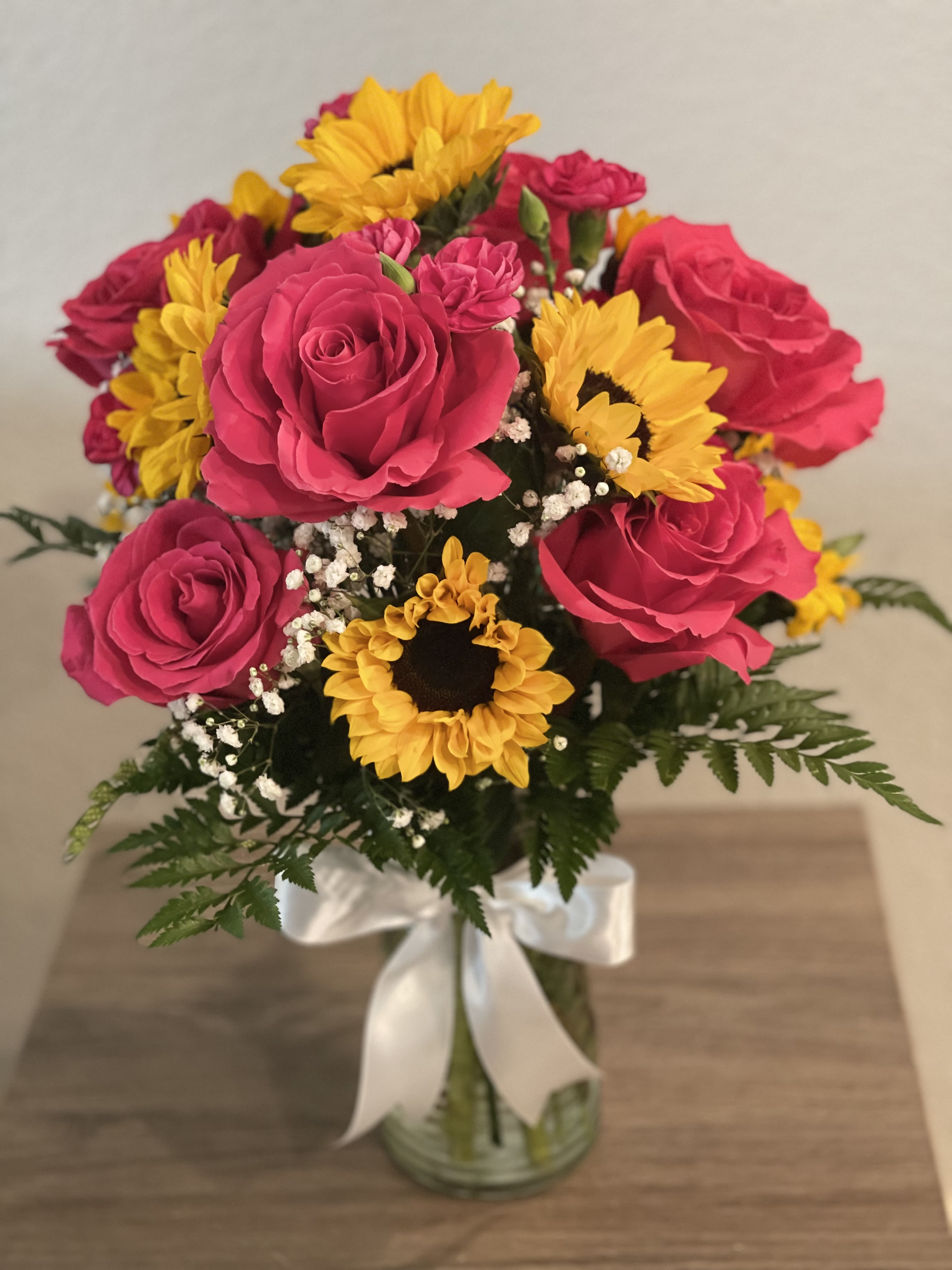 Bouquet of pink roses and yellow sunflowers in a glass vase with a white ribbon