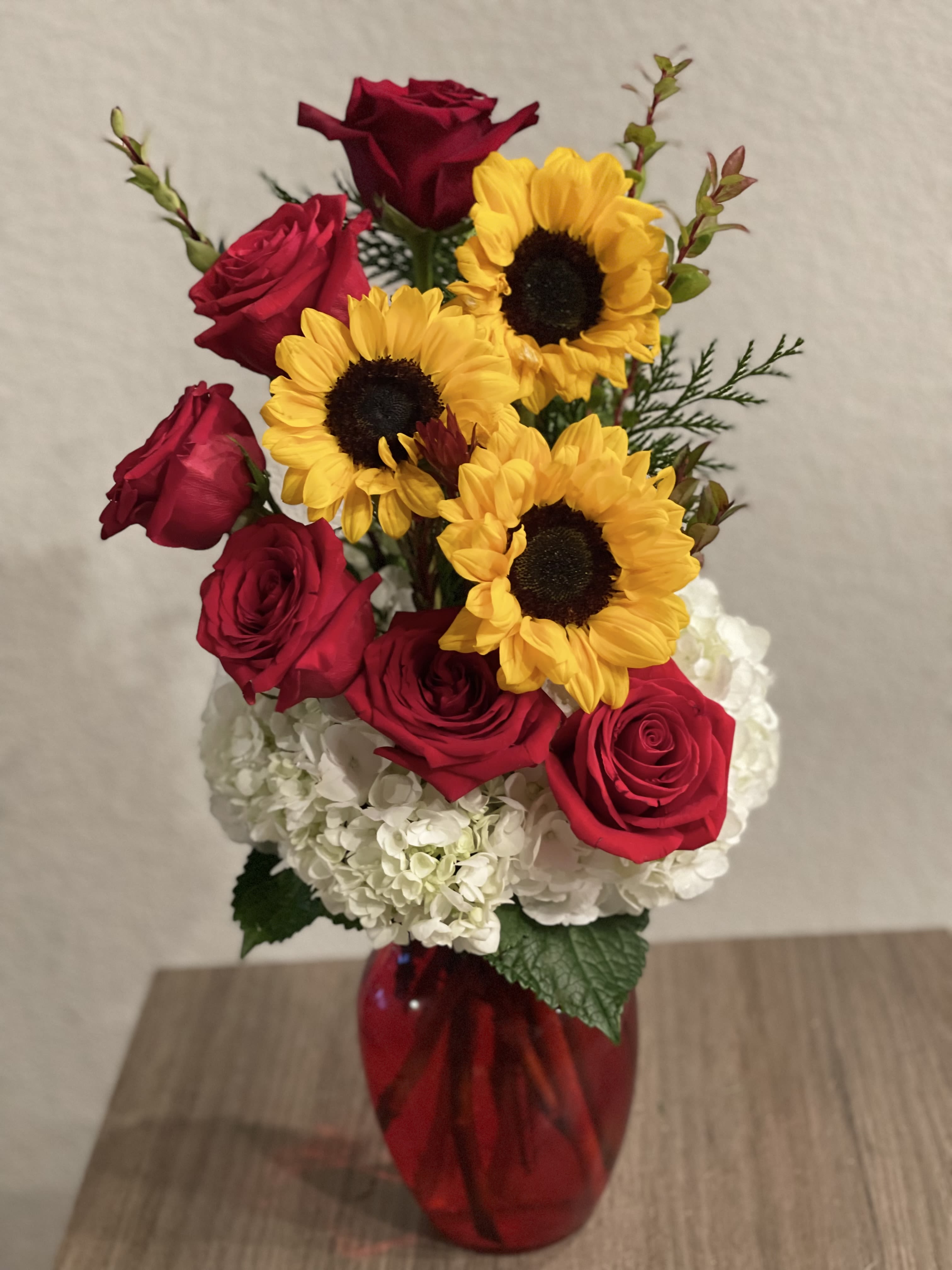 Red roses and yellow sunflowers in a red vase with white hydrangeas