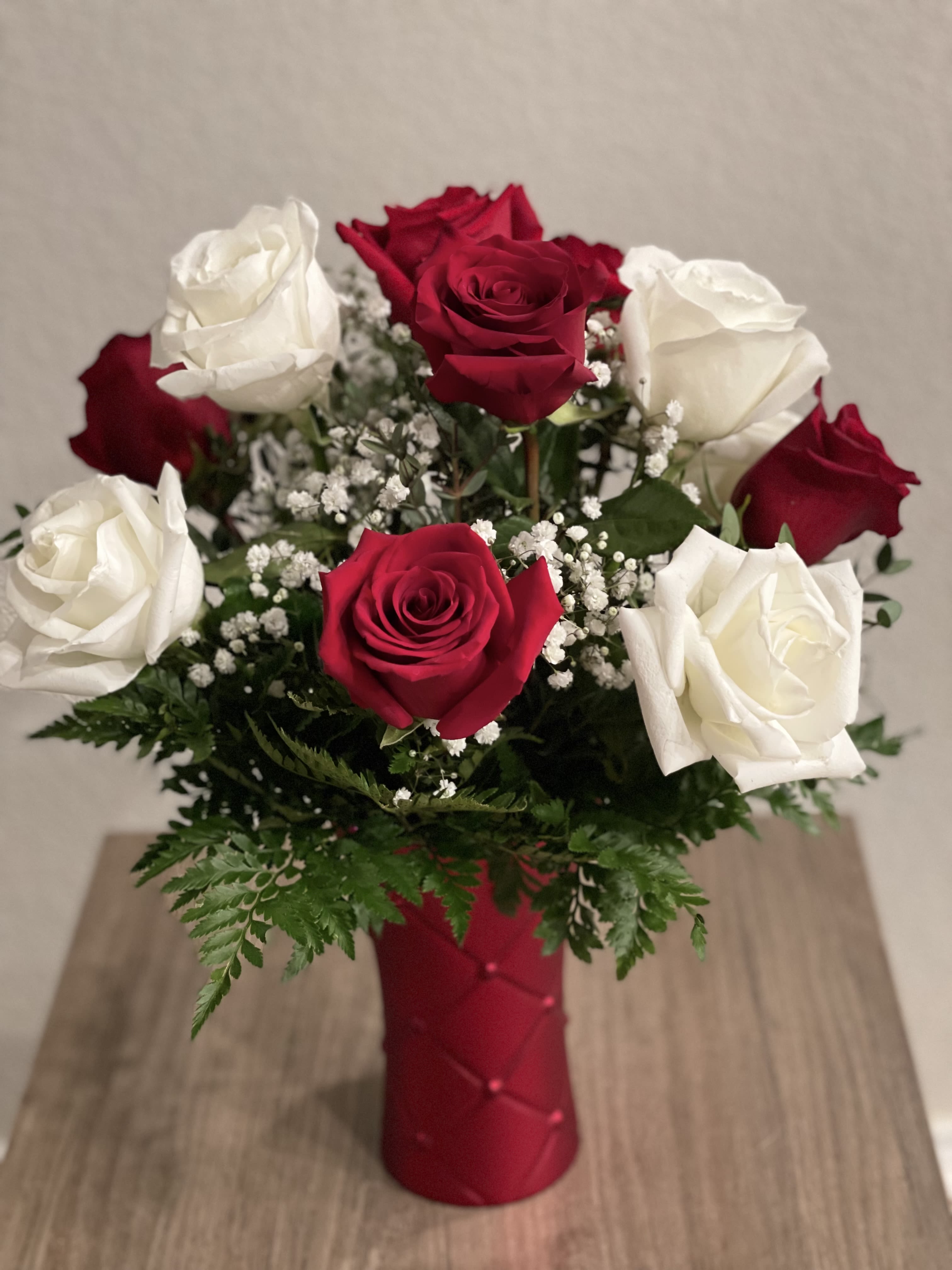 Red and white roses in a red vase with baby's breath