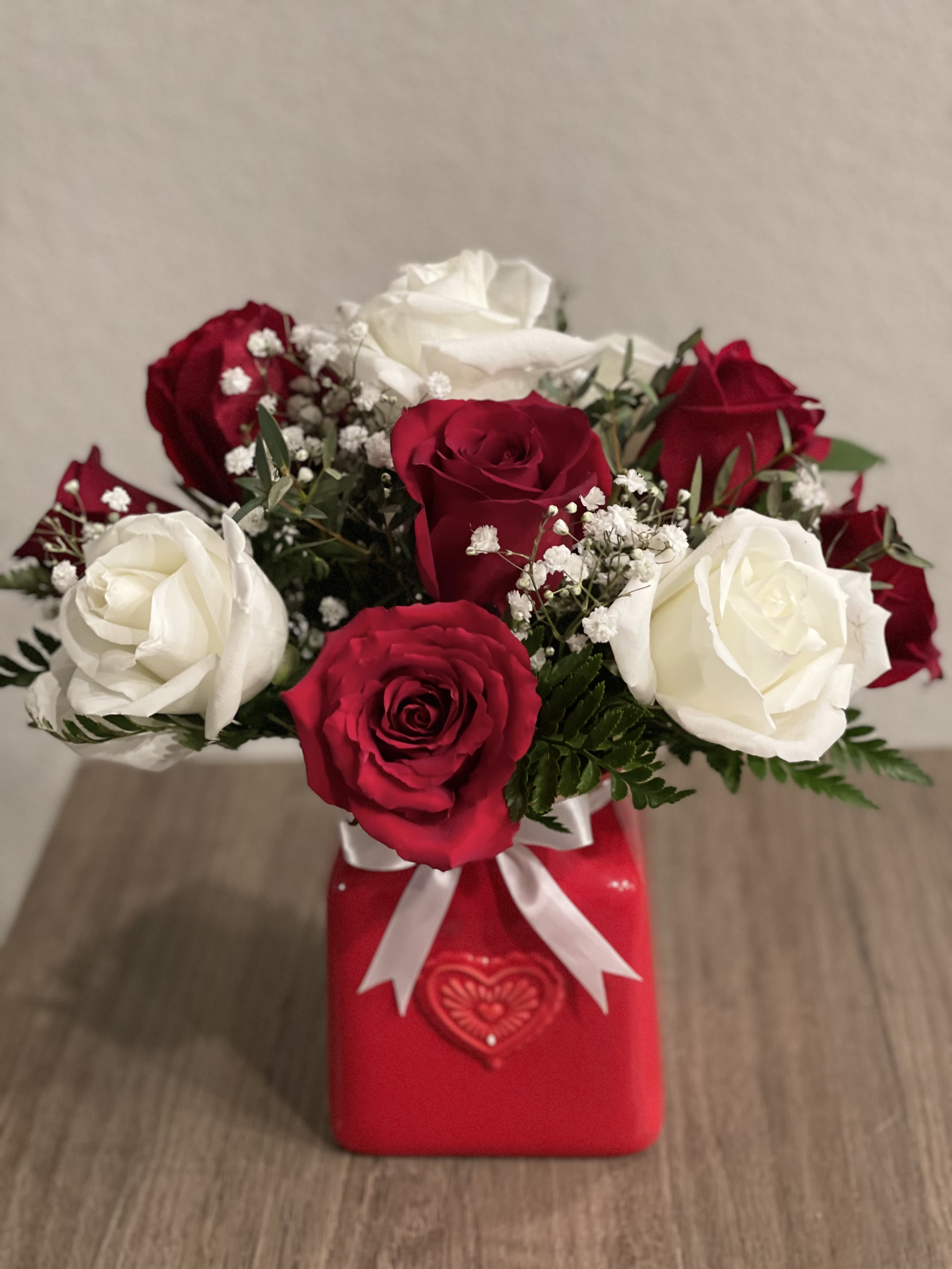 Red and white roses arranged in a red gift box with a white ribbon