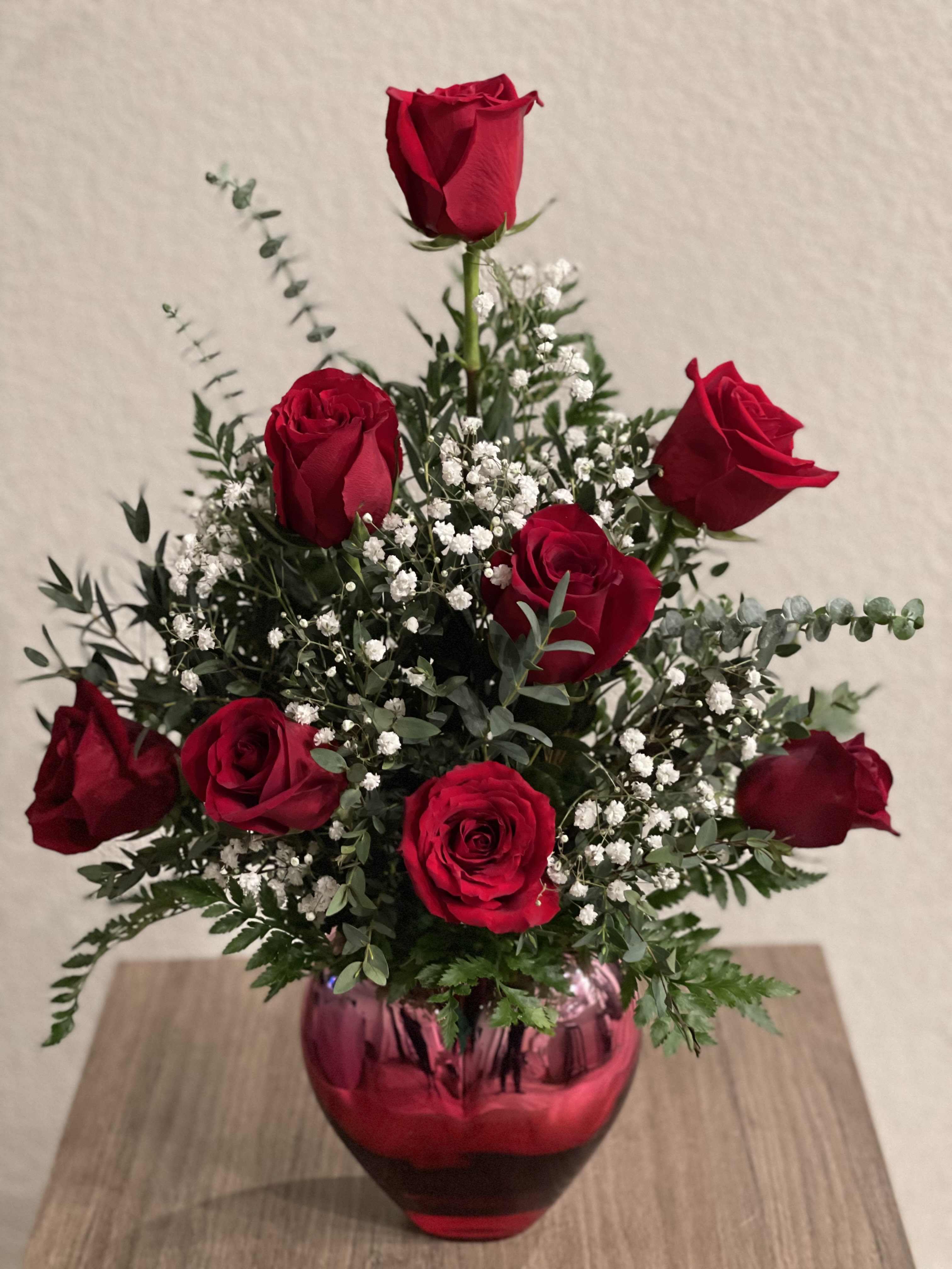 Red roses arranged in a pink glass vase with white filler flowers
