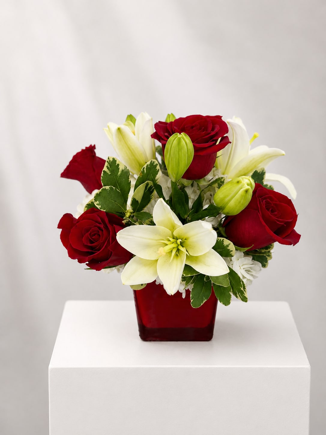 Red roses and white lilies arranged in a red square vase