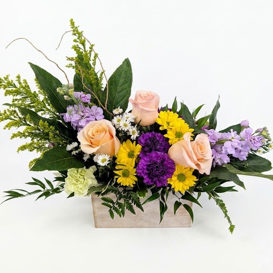 Mixed bouquet in a wooden box with peach roses, purple blooms, and yellow daisies