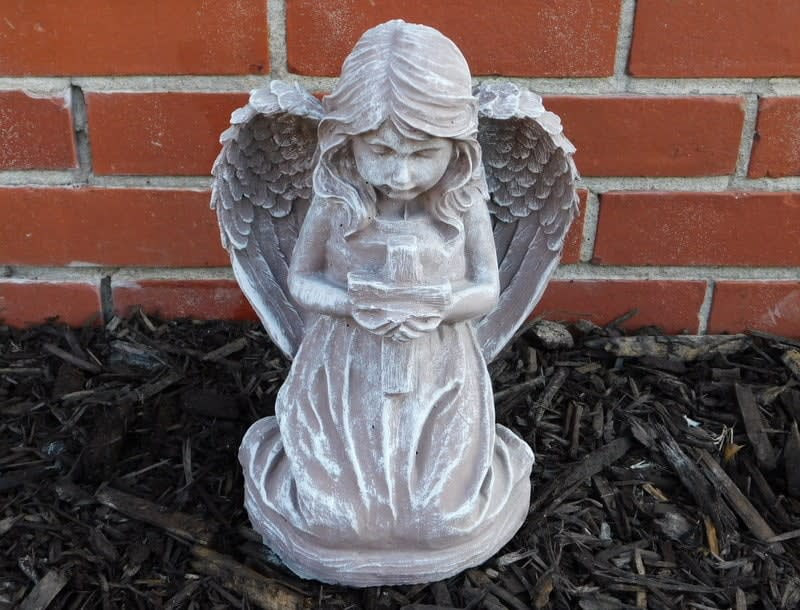 White angel statue holding a candle in front of a brick wall