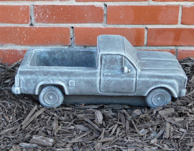 Gray pickup truck-shaped planter on mulch in front of a brick wall
