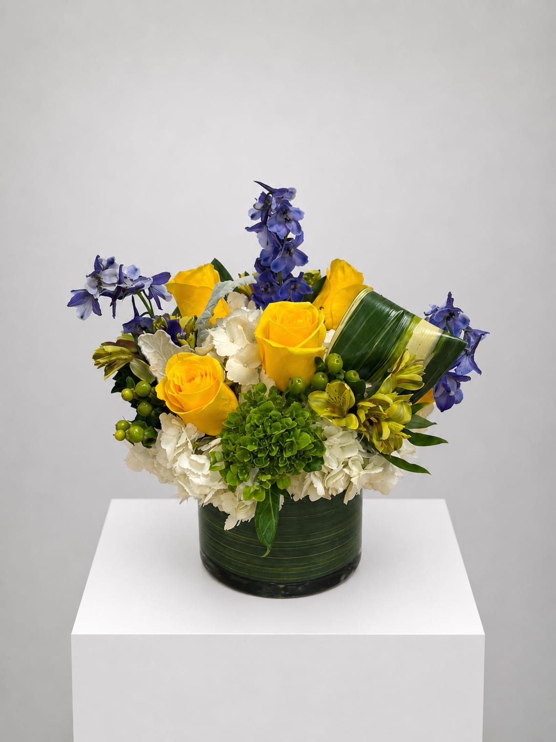 Yellow roses and blue flowers arranged in a green vase