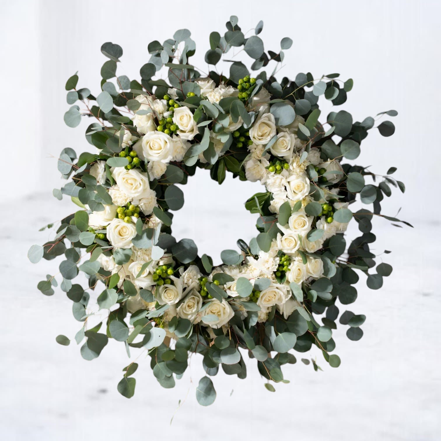 Eucalyptus Embrace Wreath - Celebrate life and honor cherished memories with the Eucalyptus Embrace Wreath. This elegant arrangement combines lush eucalyptus, white roses, and seasonal greenery to create a timeless symbol of remembrance and love. Perfect for funerals or memorial services, its natural beauty brings comfort and serenity. Handcrafted with care, this wreath is designed to convey your heartfelt sympathies. Available for delivery in Houston and surrounding areas, the Eucalyptus Embrace Wreath is an ideal choice for commemorating a loved one. With delivery to Houston and neighboring areas such as Sugar Land, Katy, and The Woodlands, this design ensures your condolences are expressed with grace and care.  Easels are included in the price of all wreath arrangements to ensure easy display at services.