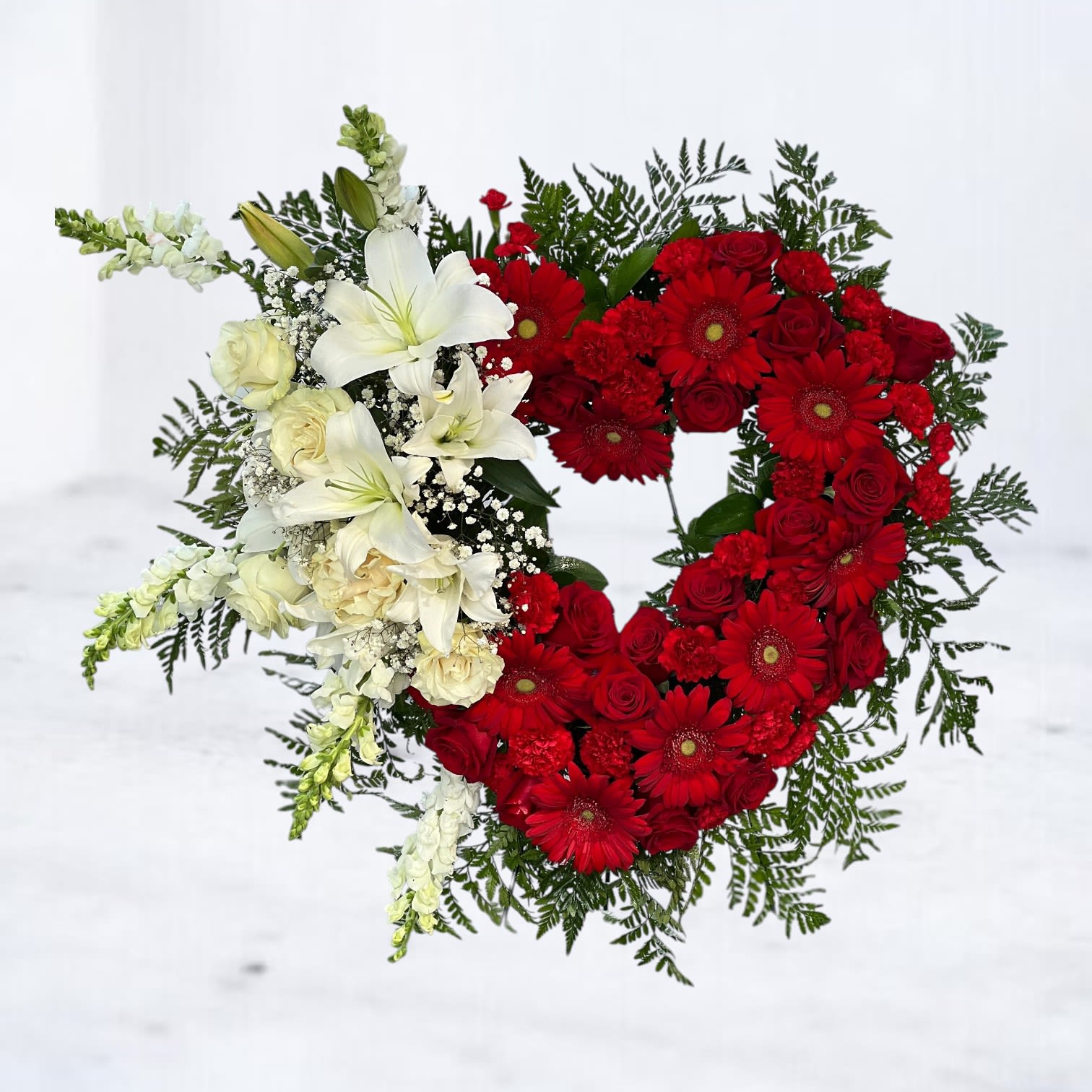 Crimson Honor Heart Wreath - A striking tribute to everlasting love and profound respect, the Crimson Honor Heart Wreath commands attention with its bold palette and symbolic form. Featuring rich red roses and gerbera daisies woven into a heart-shaped form, this arrangement is accented with cascading white lilies, roses, snapdragons, and baby's breath for a contrast that speaks volumes. Each flower is carefully placed to express strength, love, and remembrance—making this wreath a powerful centerpiece for memorials, funeral services, or celebration of life ceremonies.  This 18-inch heart wreath includes a 48" standing easel and is available for same-day delivery across Houston and the surrounding areas, including The Woodlands, Katy, Conroe, Sugar Land, Spring, and beyond. Hand-delivered to local funeral homes with care.  