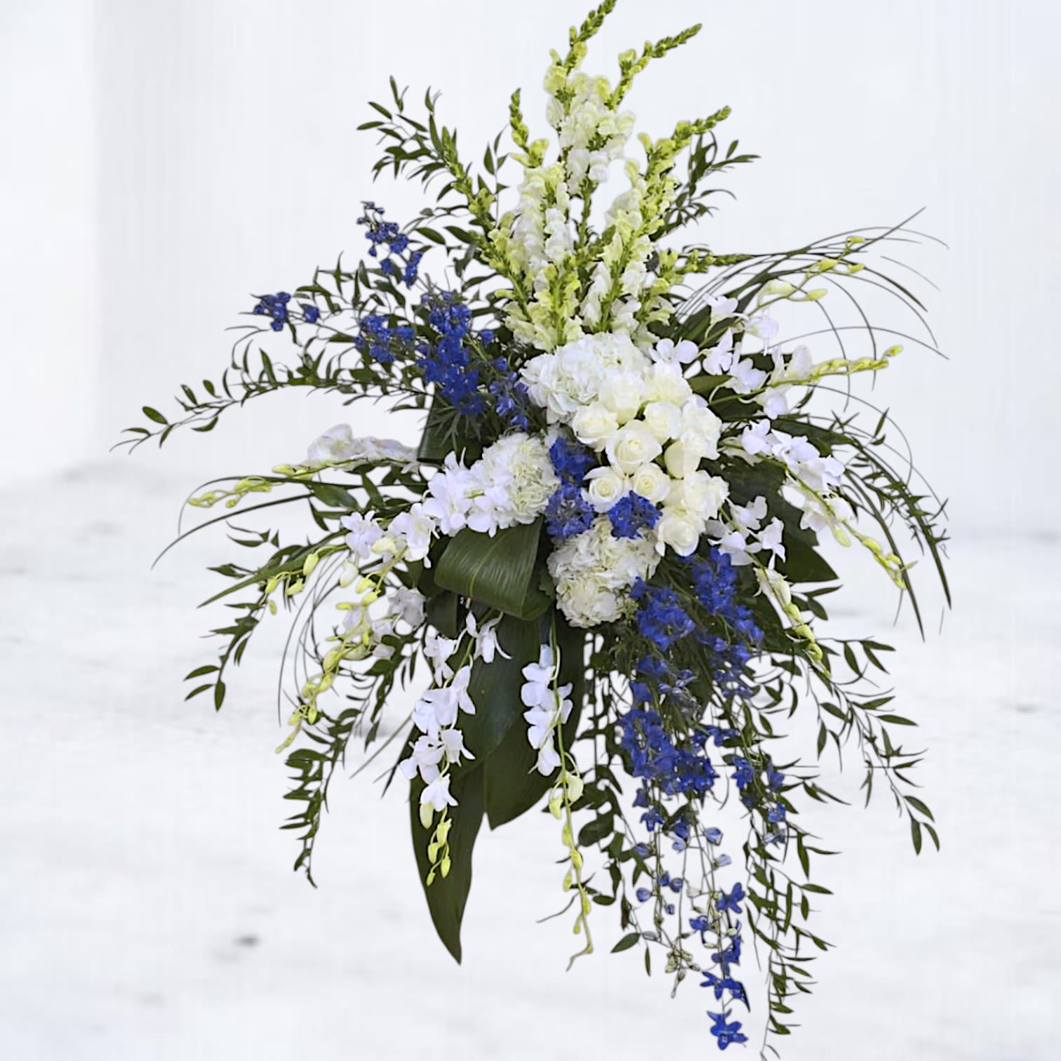 Tall floral spray with white and blue flowers and cascading greenery