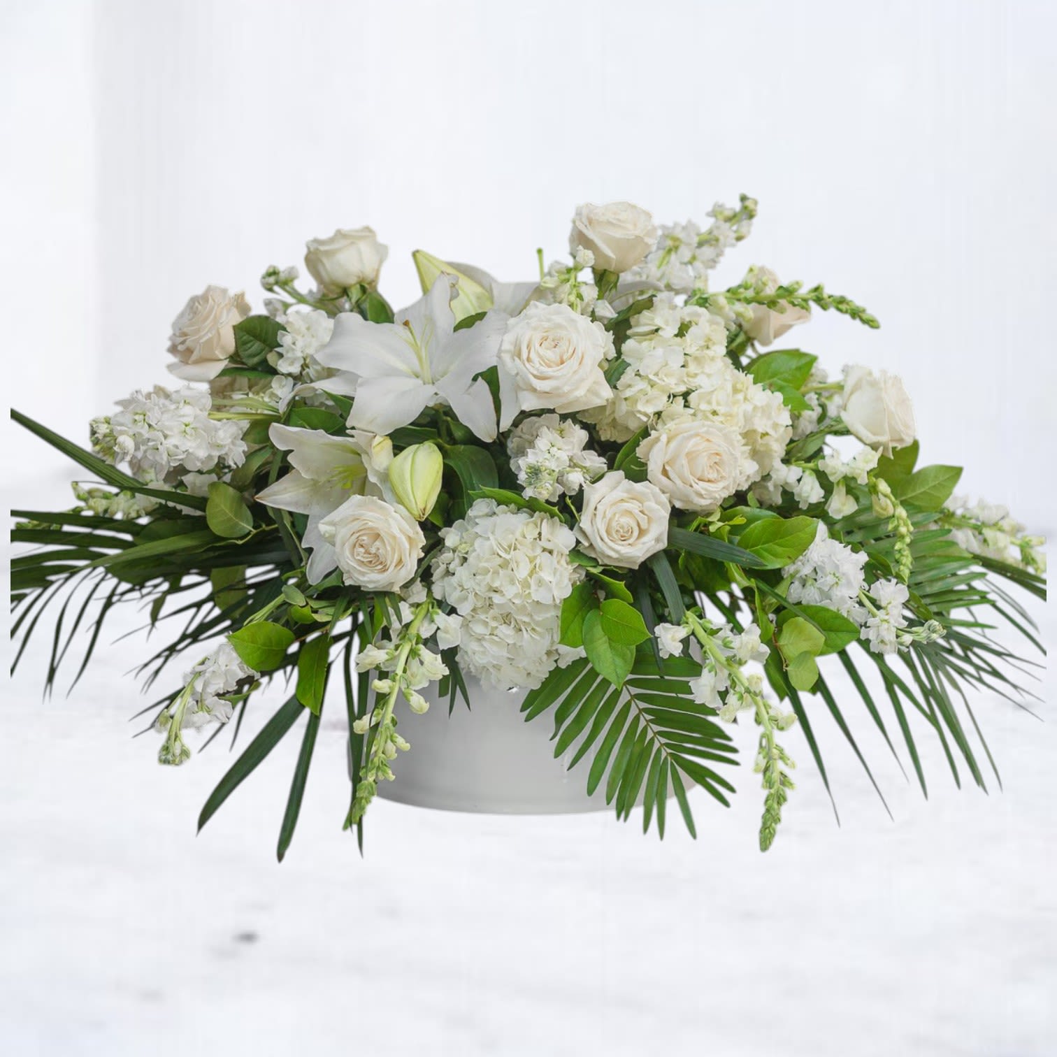 White Lotus - White Lotus is a lush all-white floral arrangement designed with layered texture, graceful movement, and modern tropical-inspired styling. Featuring premium white roses, hydrangea, lilies, stock, and seasonal white blooms accented with sculptural palm foliage and fresh greenery, this arrangement creates a clean, serene statement with a refined editorial feel.  Perfect for sympathy flowers, memorial services, celebrations of life, elegant home décor, or meaningful moments that call for understated beauty, White Lotus blends timeless white florals with contemporary design for a peaceful and elevated presentation.  Designed in a modern low vessel and crafted with premium seasonal flowers for fullness, softness, and natural movement.  Available for same-day flower delivery in Magnolia, The Woodlands, Montgomery, Conroe, Spring, Tomball, and surrounding Houston areas.