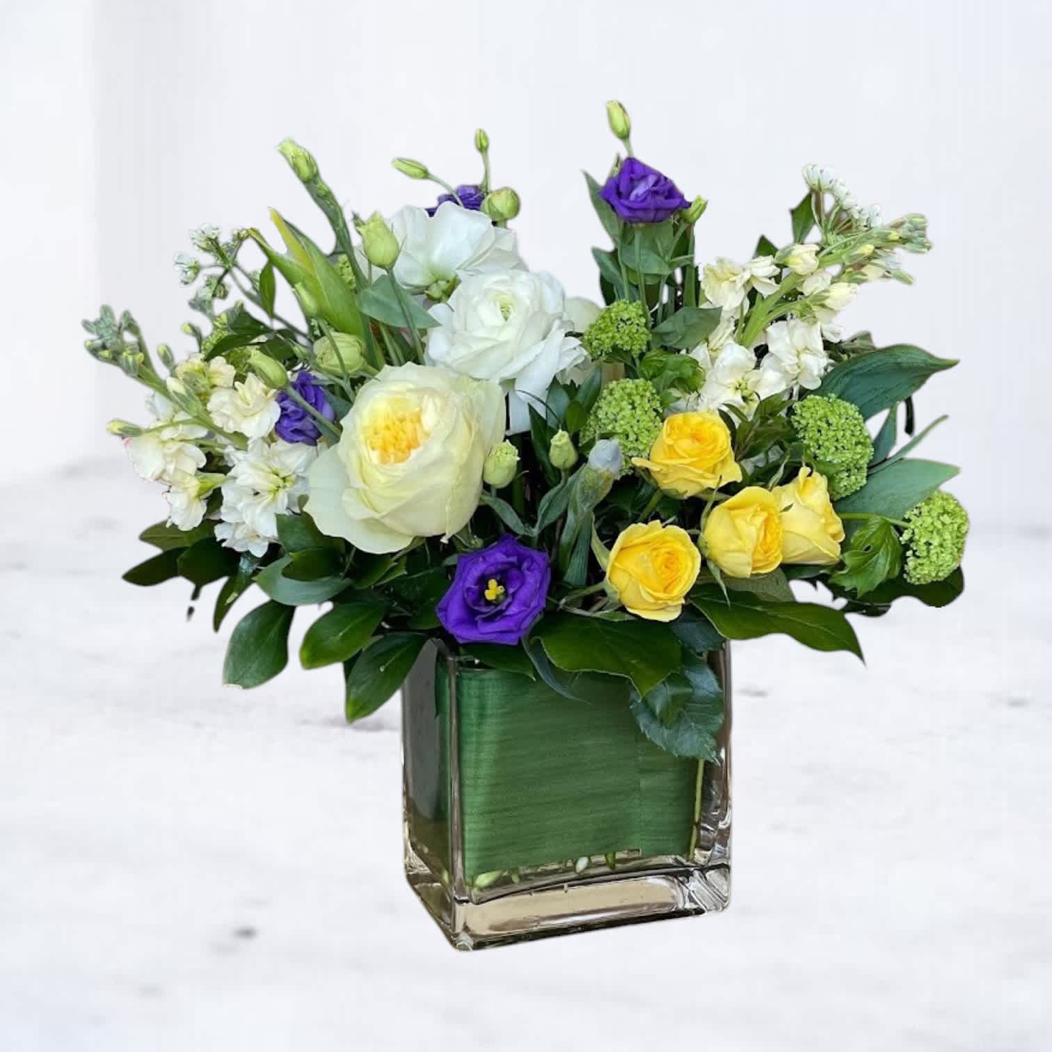 Mixed bouquet of white, yellow, and purple flowers in a square glass vase