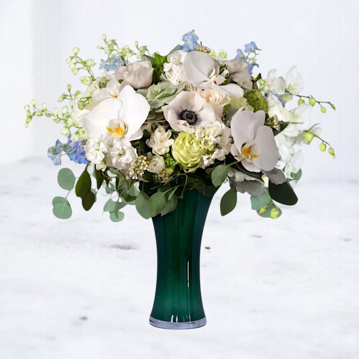 Angelic Haven Bouquet - The Angelic Haven Bouquet is a graceful blend of pure white orchids, delicate anemones, soft stock, and lush green roses, beautifully arranged in a sleek 10" tall dark green vase. This serene design symbolizes peace, comfort, and cherished remembrance, making it a meaningful tribute for sympathy occasions or to honor a life well-lived.  Why You'll Love It: Features premium blooms like Phalaenopsis orchids and anemones for an elegant touch. Soft white and green tones offer a calming, heartfelt sentiment. A timeless arrangement perfect for memorials, sympathy gestures, or thoughtful remembrance.  Whiskey Wallflower is a design-forward florist serving Magnolia, The Woodlands, Montgomery, Willis, Conroe, Spring, Tomball and surrounding Houston-area communities. We specialize in thoughtfully composed, modern floral arrangements with a focus on premium blooms, intentional design, and reliable same-day delivery. Every piece is created with care to make life’s moments feel elevated, personal, and unforgettable.