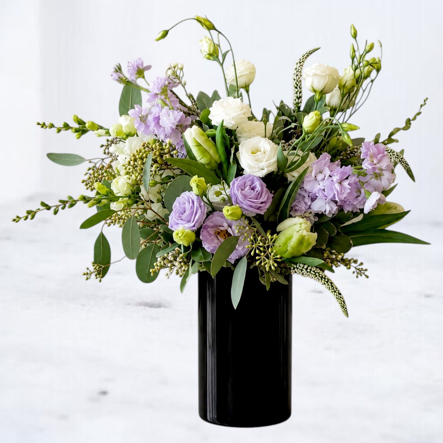 Wisteria - Wisteria is a modern garden-inspired arrangement featuring soft lavender blooms, creamy white roses, and layered seasonal greenery arranged in a sleek dark glass vase. Designed with airy movement and natural texture, this composition captures the relaxed elegance of a flowering garden in full bloom.  The gentle violet palette paired with lush greenery creates a refined yet effortless look, making Wisteria House a beautiful choice for birthdays, thank-you gifts, celebrations, or simply bringing fresh botanical beauty into the home.  Whiskey Wallflower is a design-forward florist serving Magnolia, The Woodlands, Montgomery, Willis, Conroe, Spring, Tomball and surrounding Houston-area communities. We specialize in thoughtfully composed, modern floral arrangements with a focus on premium blooms, intentional design, and reliable same-day delivery. Every piece is created with care to make life’s moments feel elevated, personal, and unforgettable.