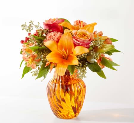 Orange and pink mixed bouquet in an amber glass vase
