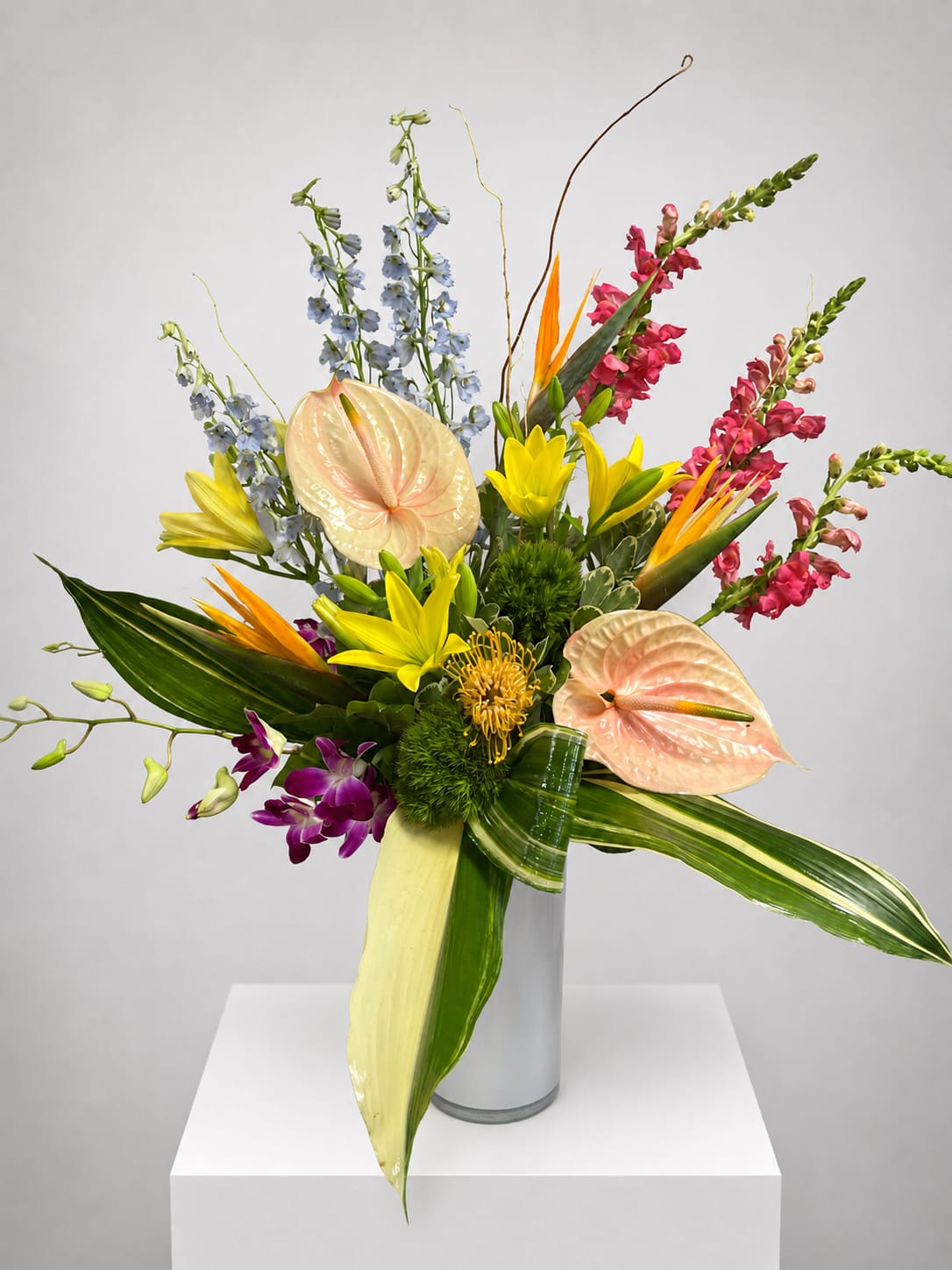 Tropical bouquet with anthuriums, orchids, lilies, and snapdragons in a glass vase